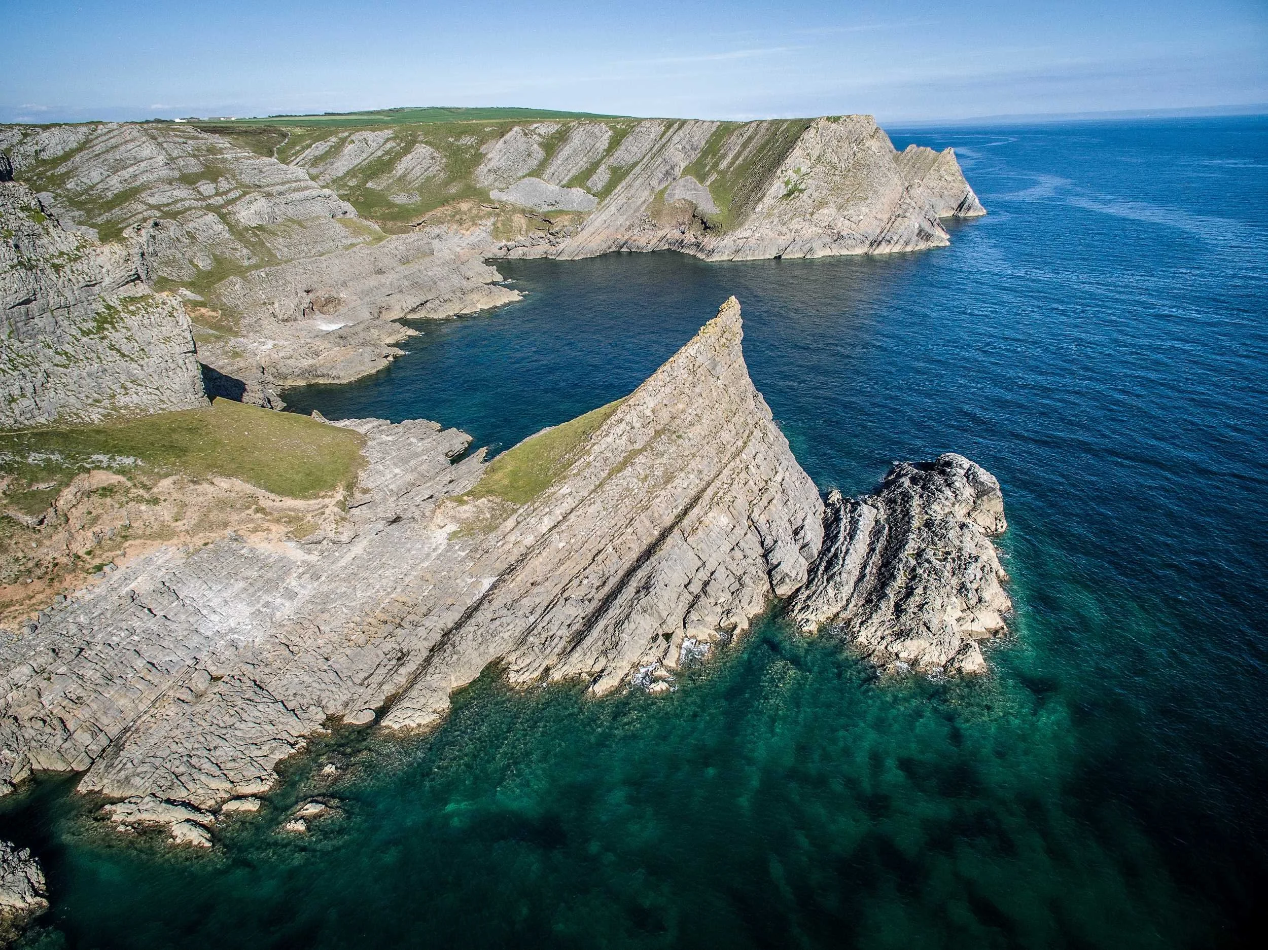 Cliffs and rocky shoreline along a blue ocean under a partly cloudy sky.