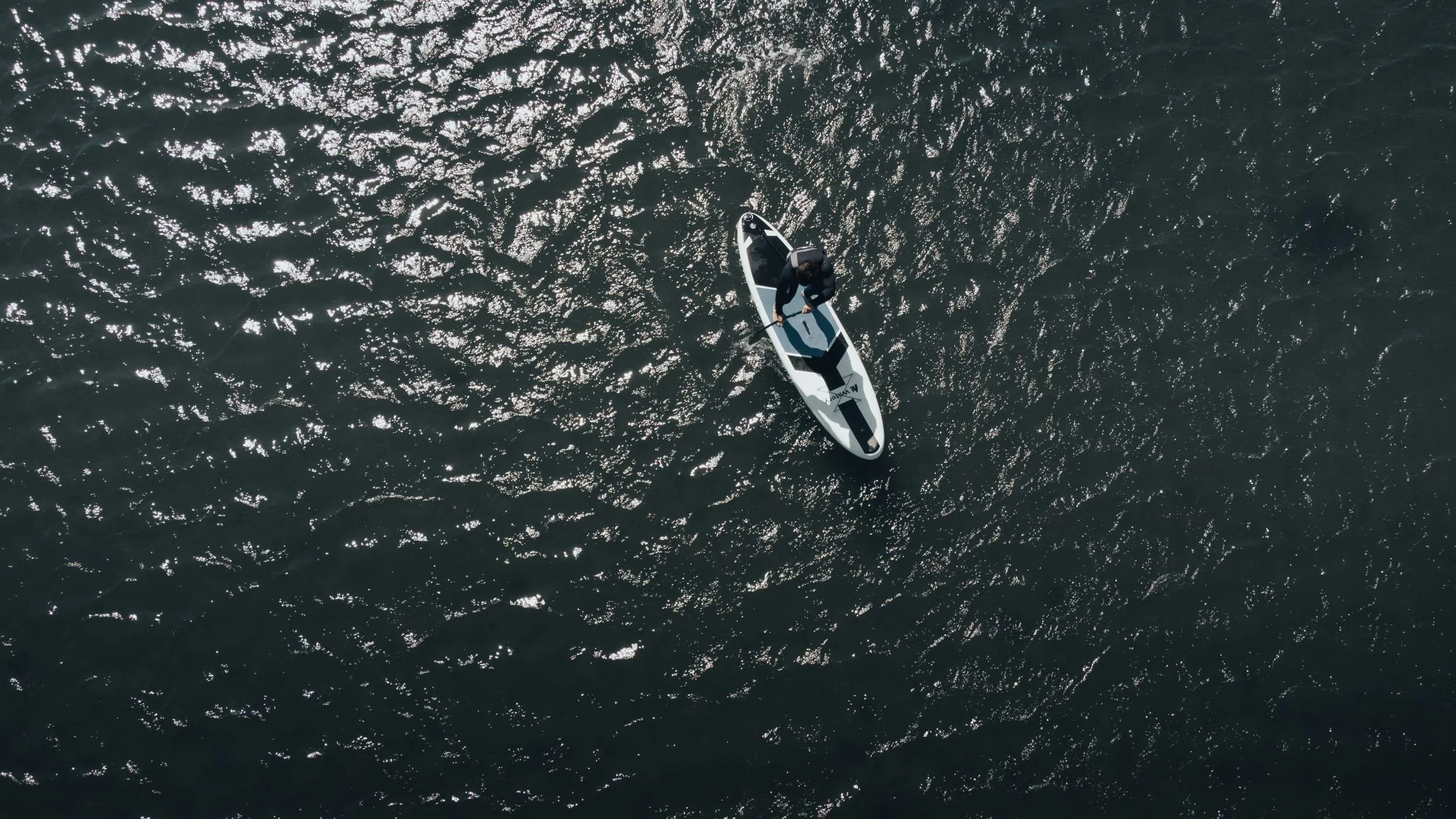 A person standing on a paddleboard in the water, viewed from above.