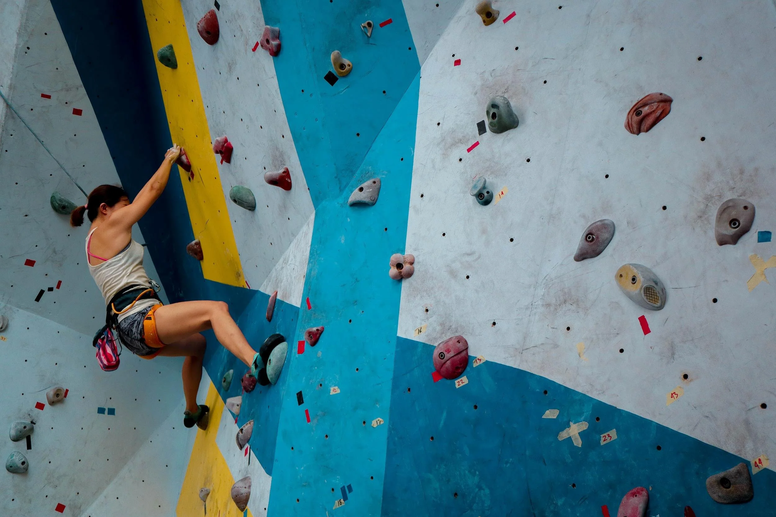 A woman rock climbing on an indoor climbing wall with colorful holds.