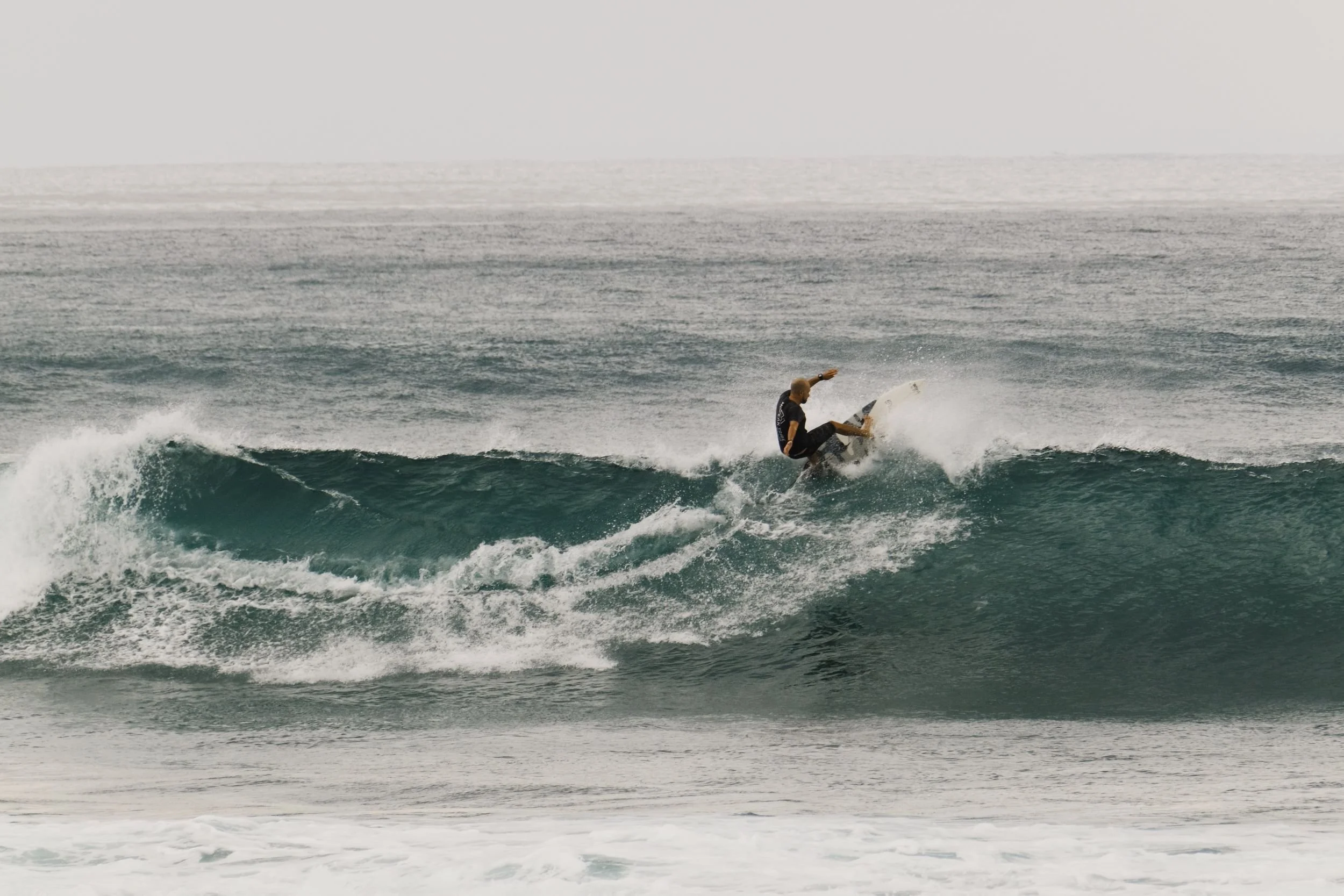 Skateboarder performing a trick on a wave at the beach.