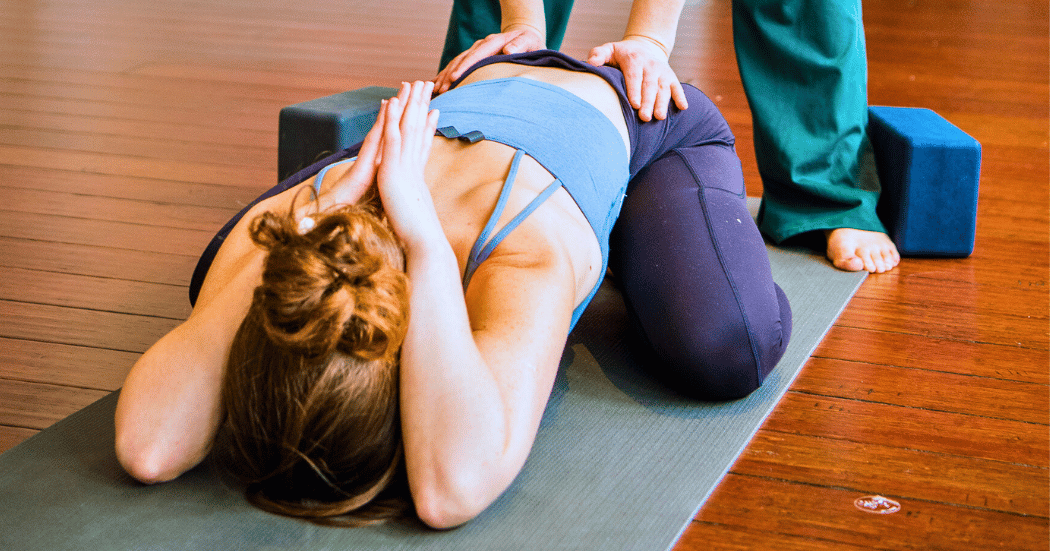 Woman practice yoga at Boston Yoga Union in Coolidge Corner with hands on assists in childs pose