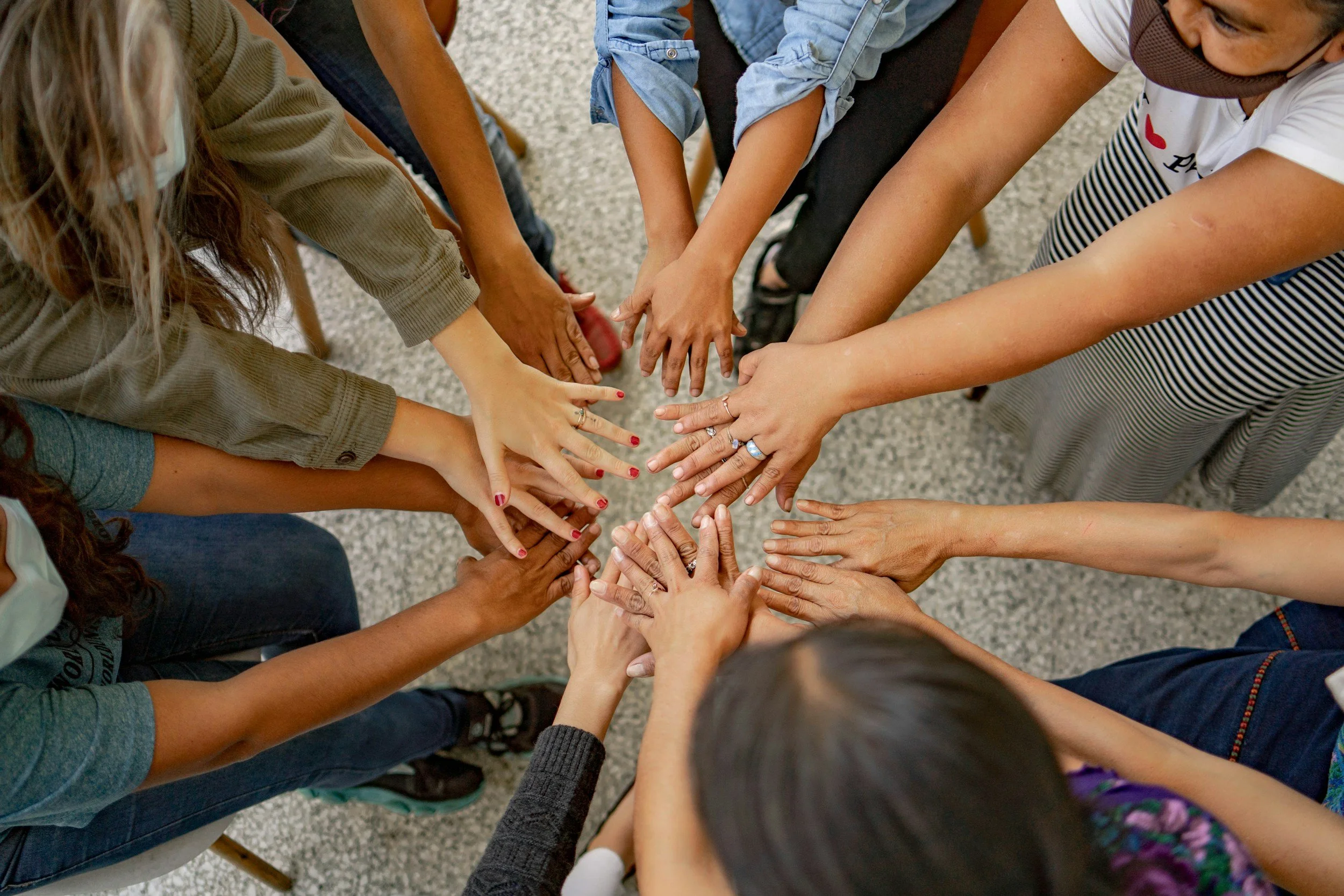 A group of diverse people with various skin tones joining their hands together in the center, forming a circle as a gesture of unity and teamwork.