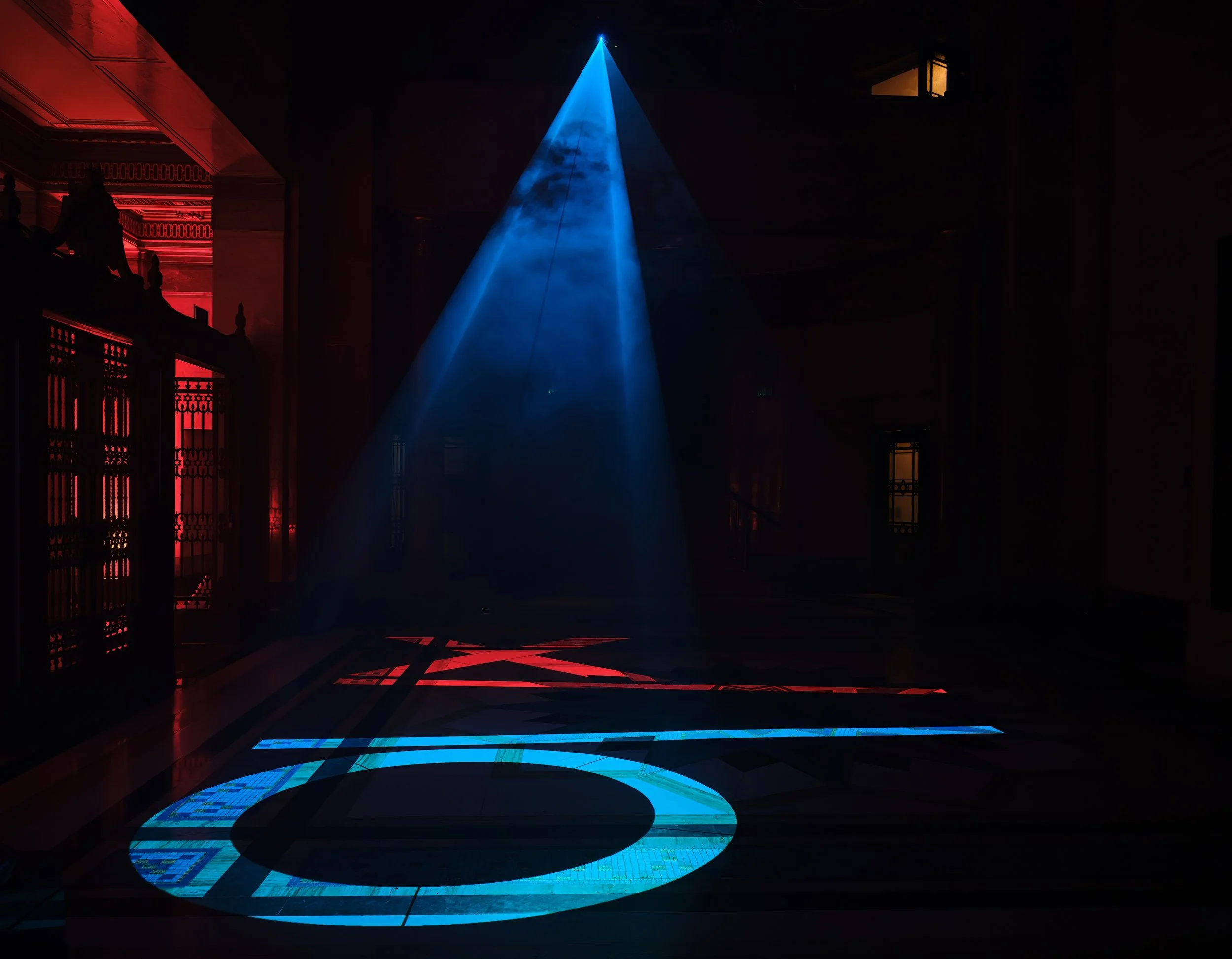 Squid Game's iconic circle, triangle, and square symbols projected dramatically on the floor with spotlights.