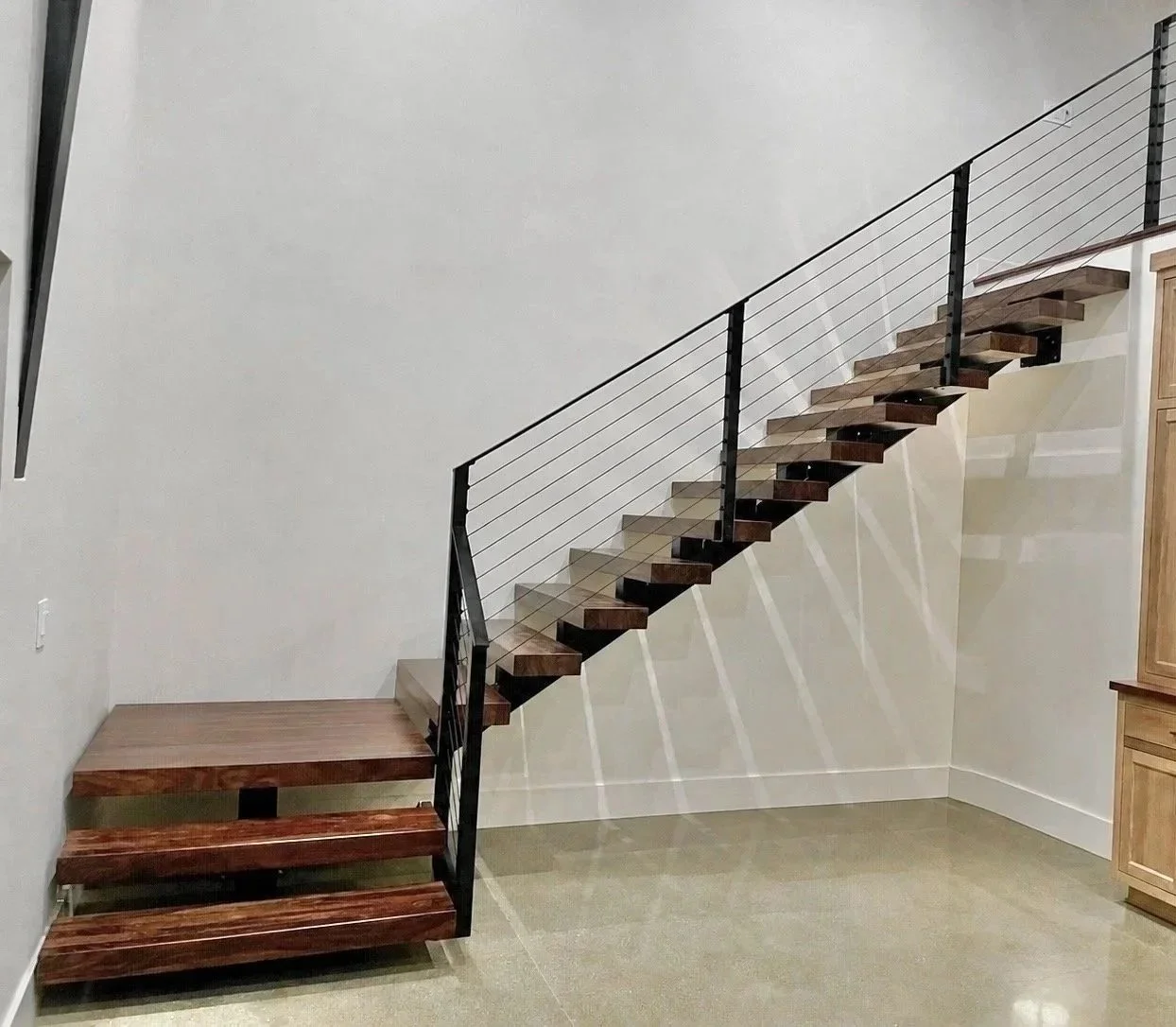 A modern staircase with wooden steps and a metal railing, leading to the upper level of a home with minimalist decor