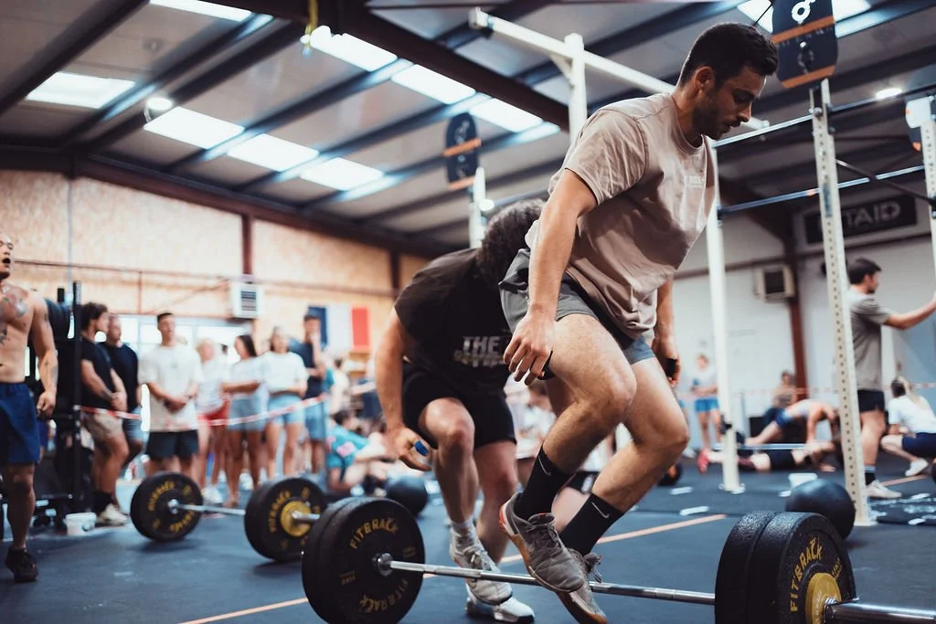 Homme effectuant un saut en levant une barre de musculation lors d'un entraînement ou compétition dans une salle de sport.