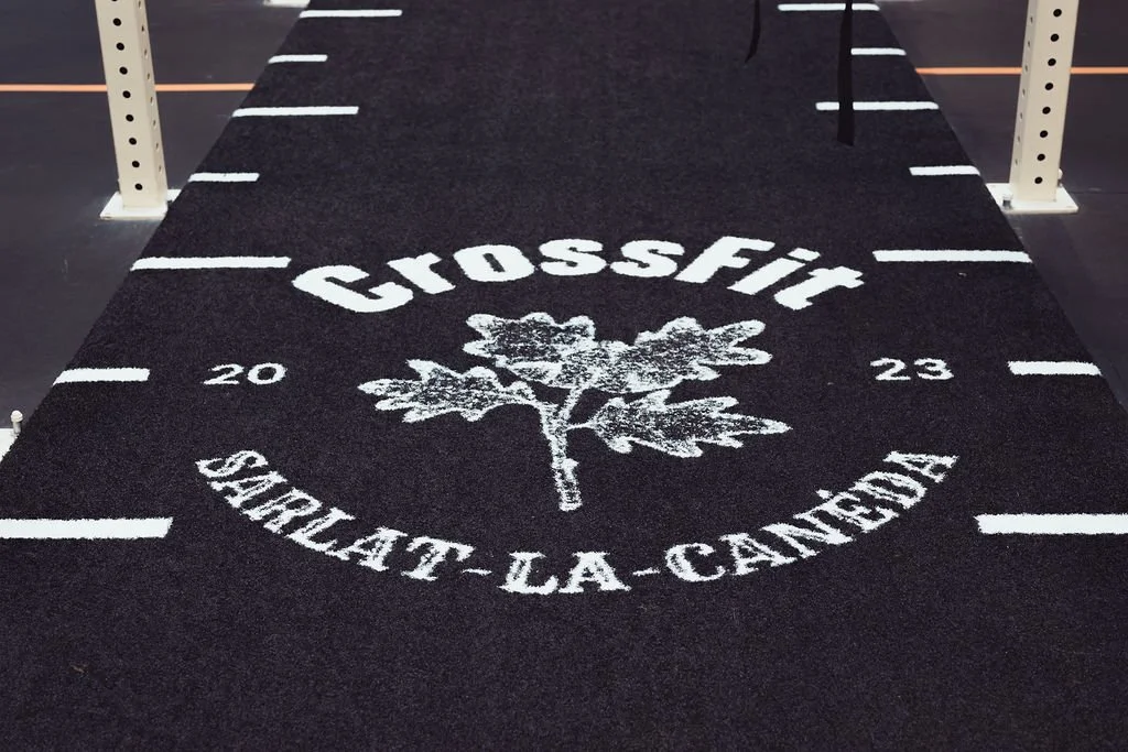 Tapis de sol de CrossFit avec logo d'une branche de chêne, texte 'CROSSFIT SARLAT-LA-CANEDA', année 2023, située dans une salle d'entraînement.