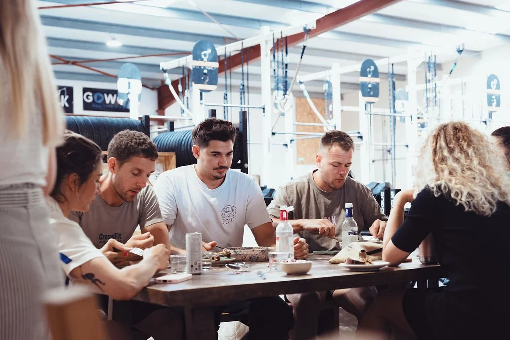 Groupe de personnes assises autour d'une table en train de manger dans une salle de sport.