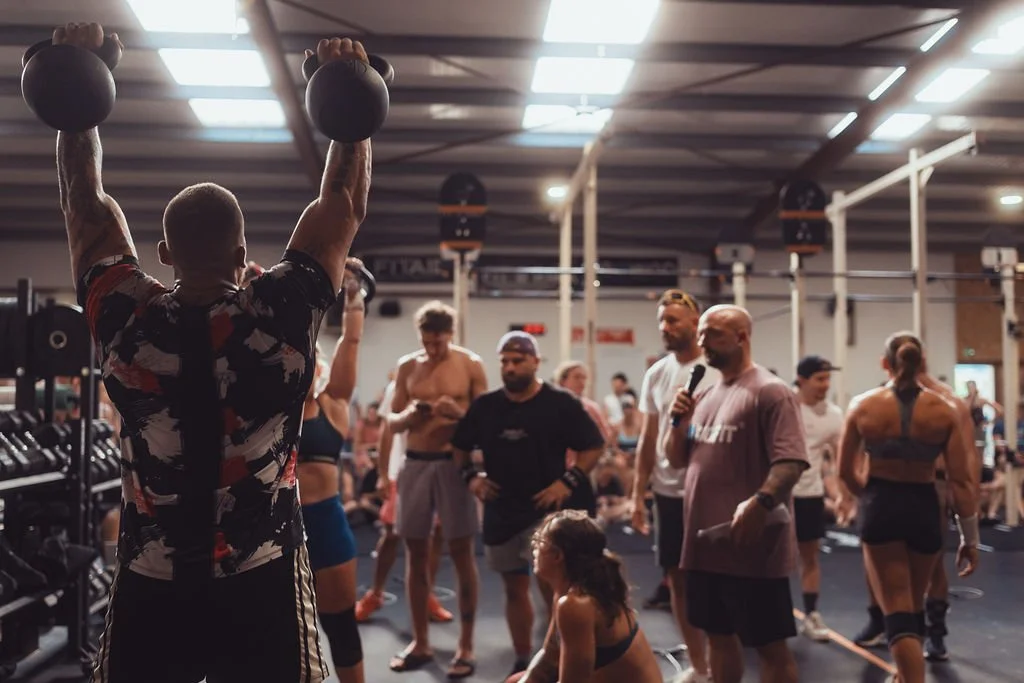Groupe de personnes dans une salle de musculation, certains en train de s'entraîner et d'autres observant, sous un plafond éclairé.