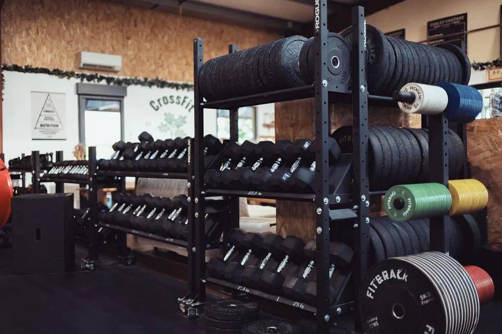 Rack de matériel de musculation avec poids, haltères, et rouleaux de fitness dans une salle de gym.