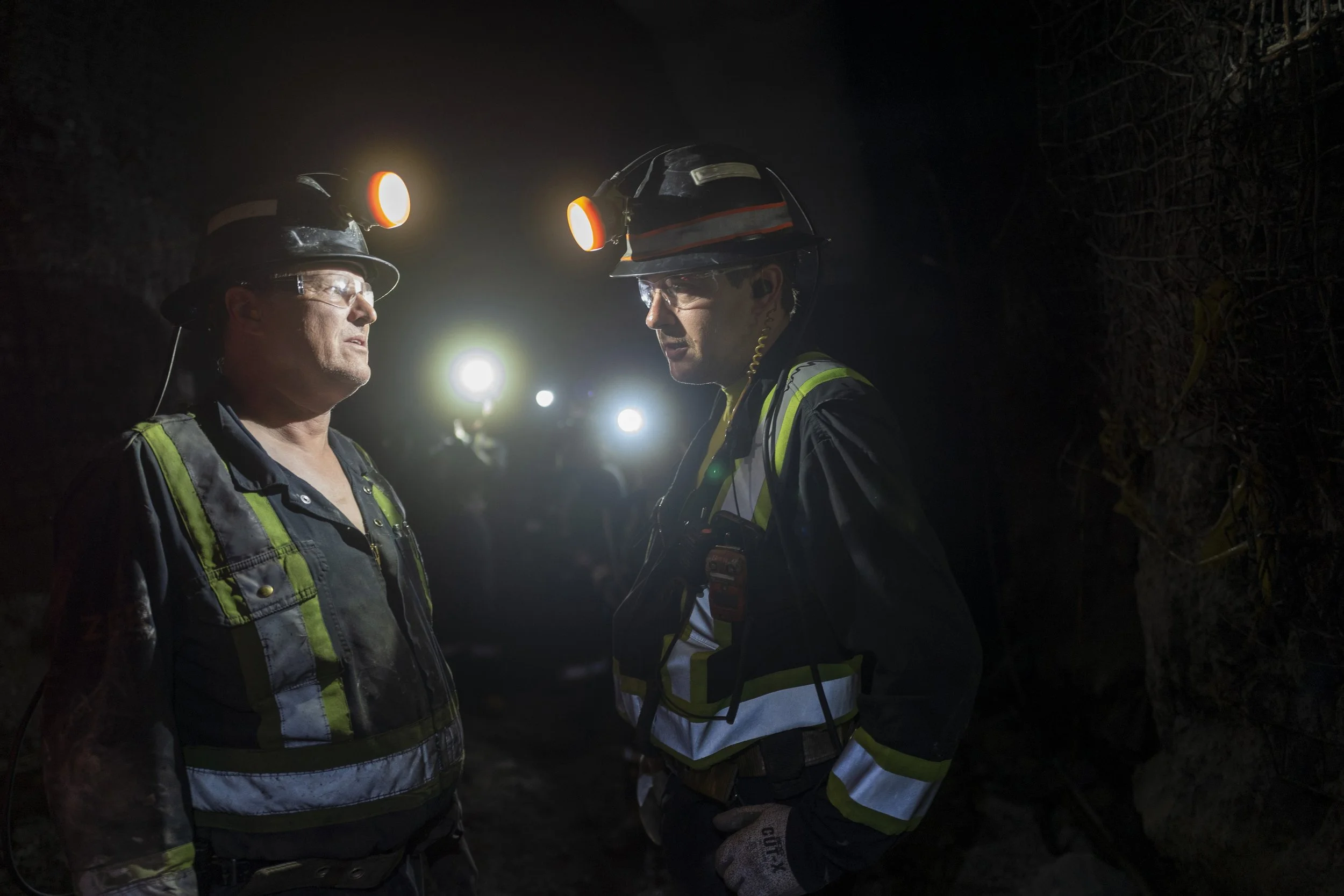 Two rescue workers wearing helmets and reflective safety vests are standing in the dark, illuminated by their headlamps.