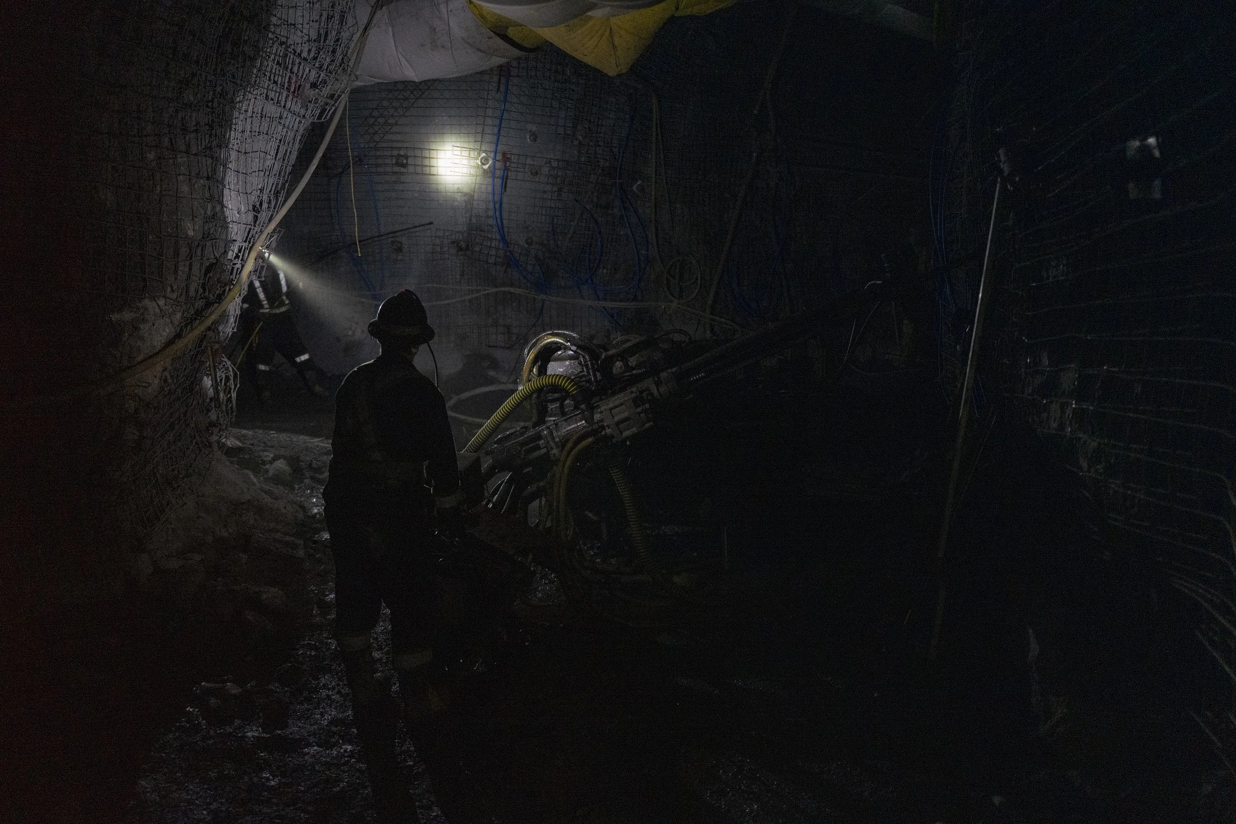 Firefighters working inside a dark tunnel, illuminated by a few lights, with equipment and netting on the walls.