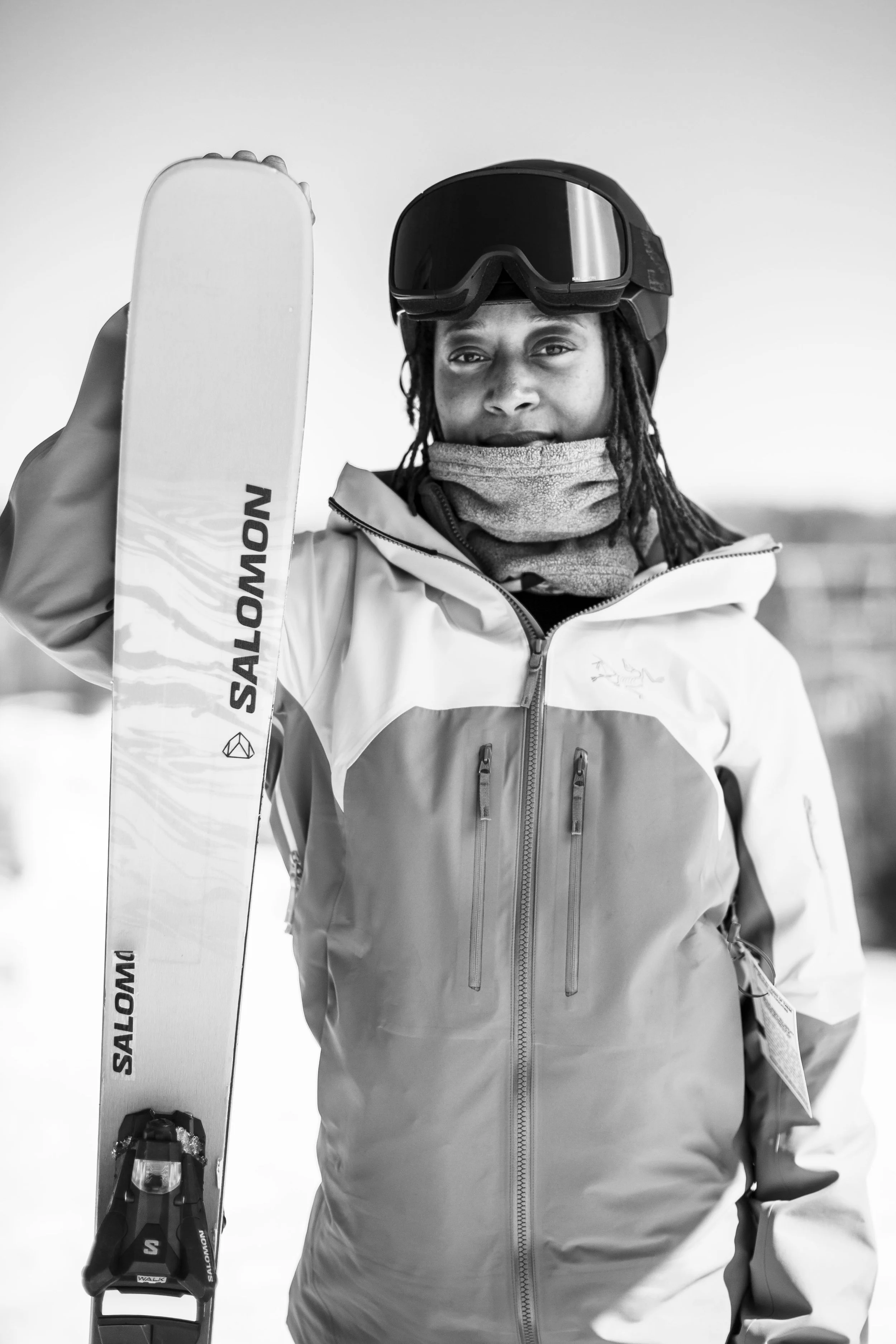 A person wearing a ski helmet and goggles holding a ski pole, dressed in a winter jacket, outdoors in a snowy environment.