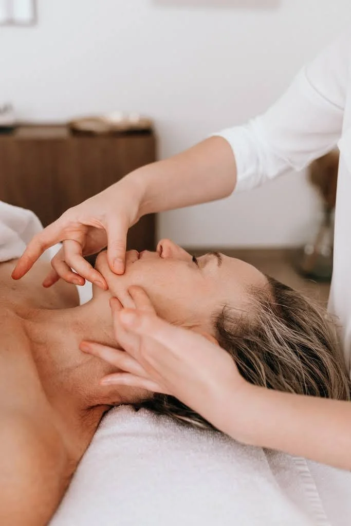 Une personne reçoit un massage du visage par un praticien dans un cadre professionnel.
