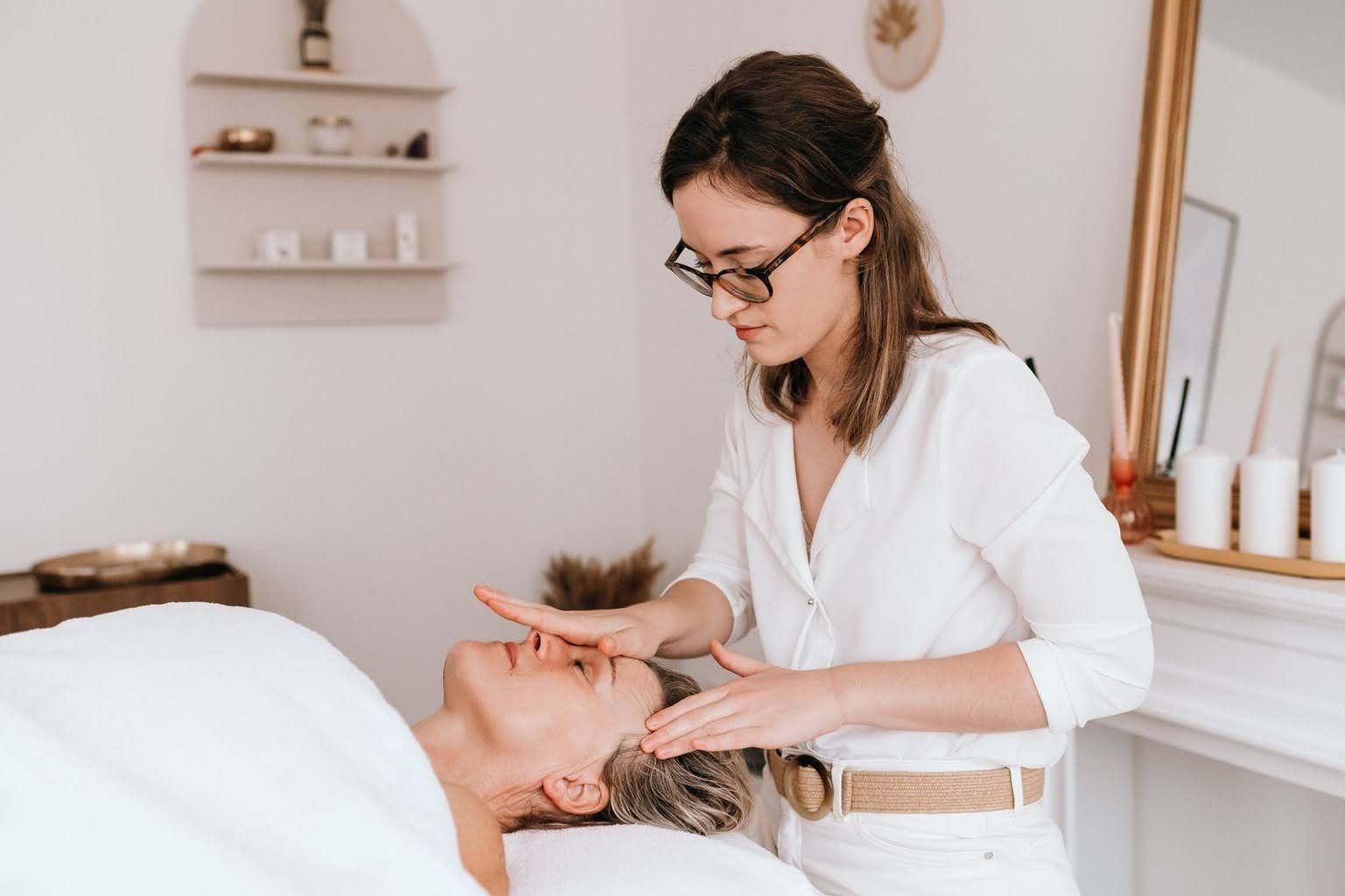 Une praticienne effectue un soin du visage à une femme couchée, dans un cabinet de soins esthétique.