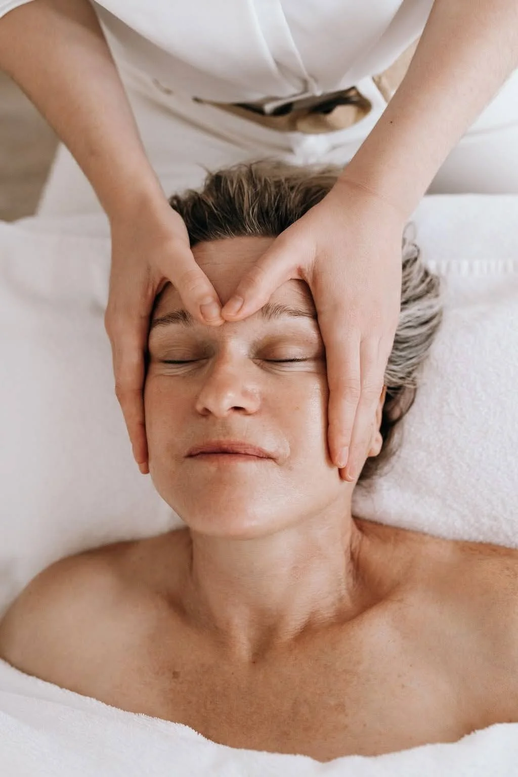 Une personne reçoit un massage du visage dans un spa, allongée sur une table, avec les yeux fermés.
