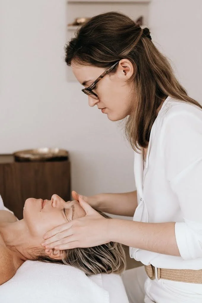 Une femme effectue un soin du visage ou un massage facial à une autre femme allongée.