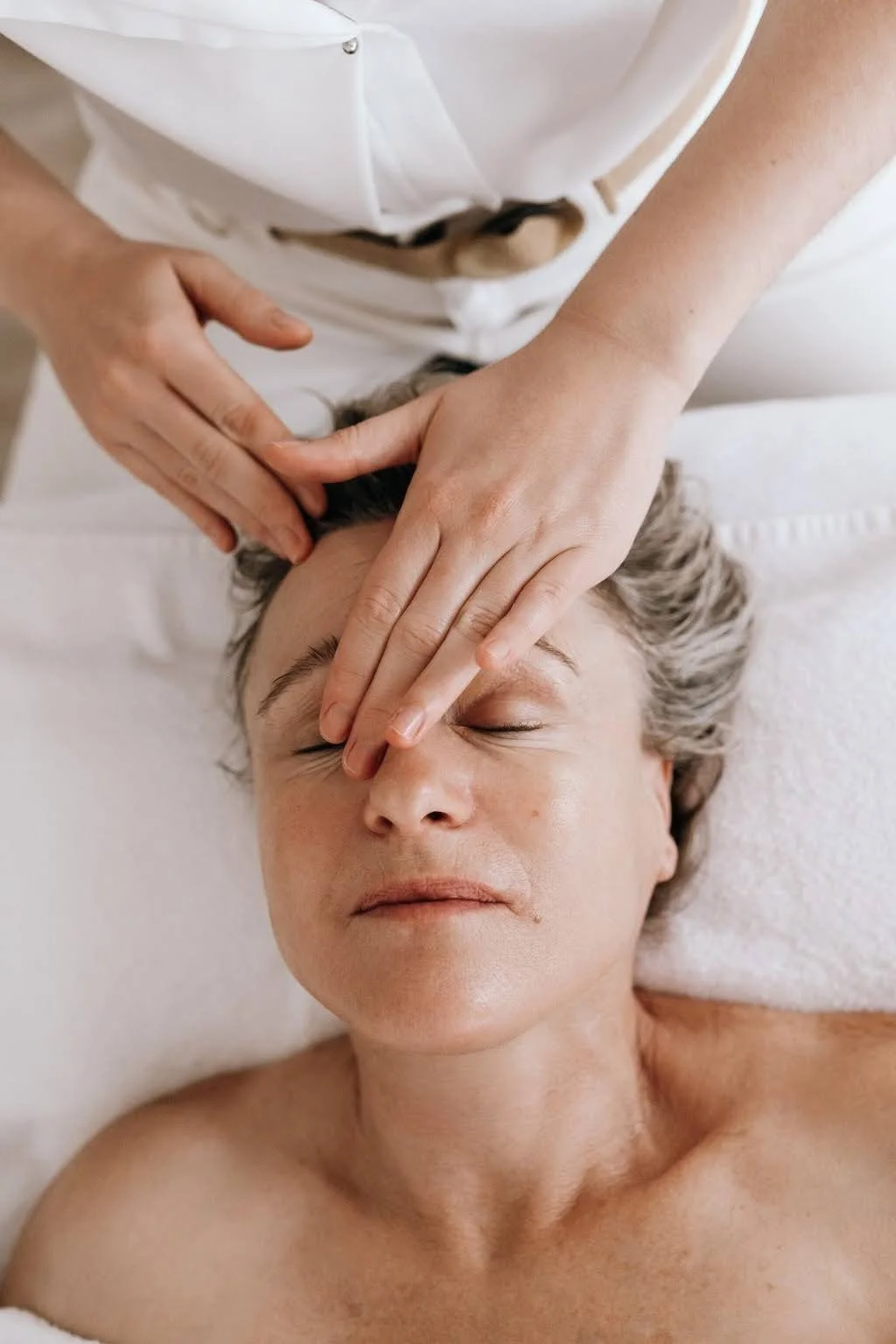 Une personne reçoit un massage du visage d'une praticienne dans un cadre relaxant.