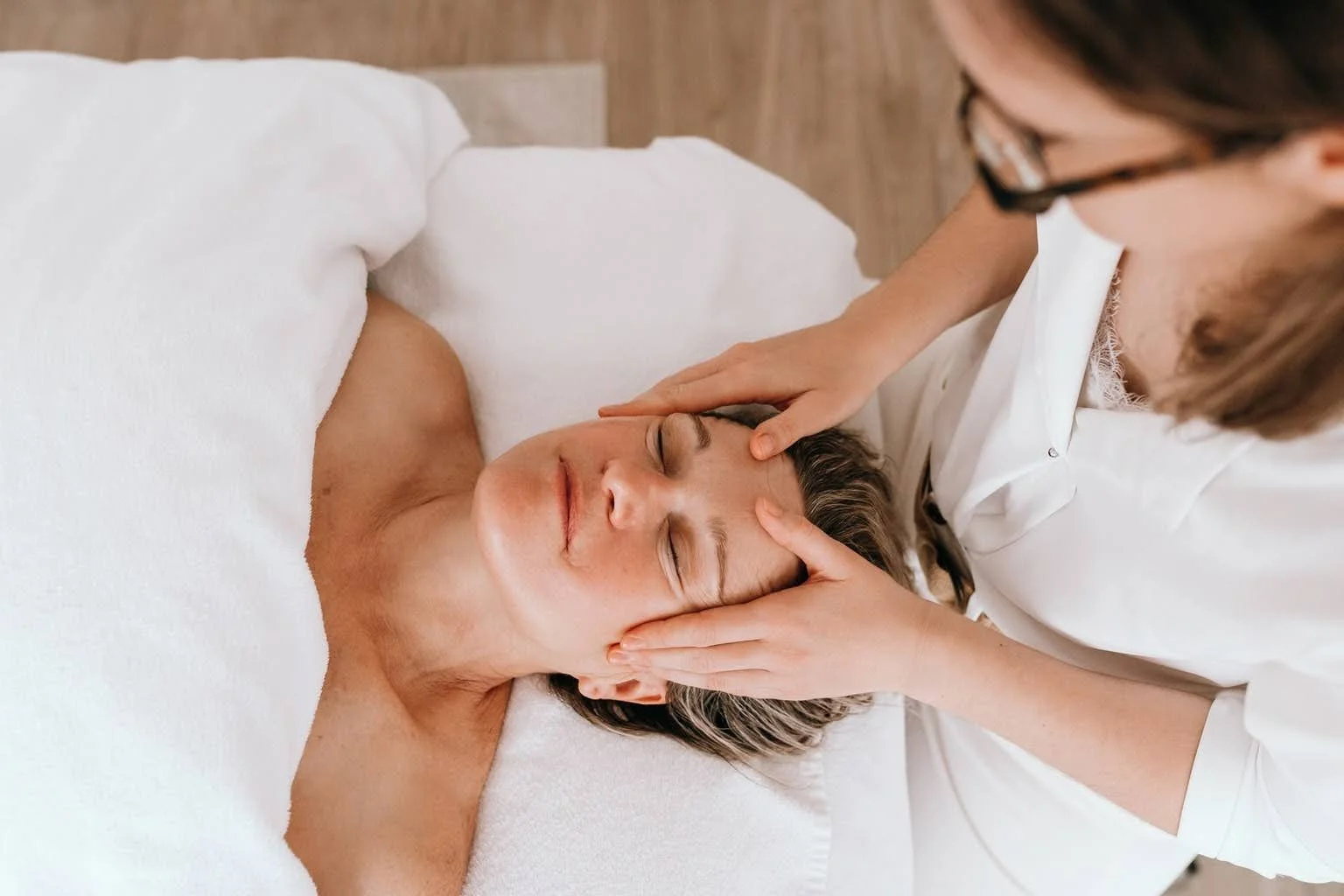 Une femme reçoit un massage du visage par un thérapeute dans un cadre relaxant.