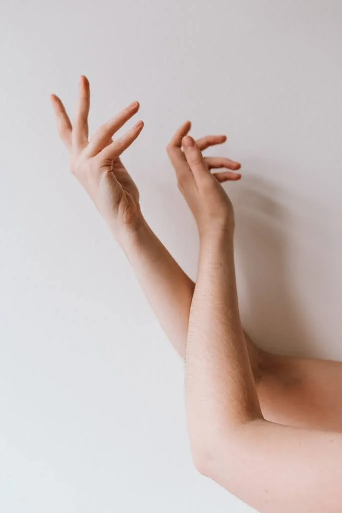 Deux bras qui se croisent, avec une main levée et l'autre pliée, contre un mur blanc.
