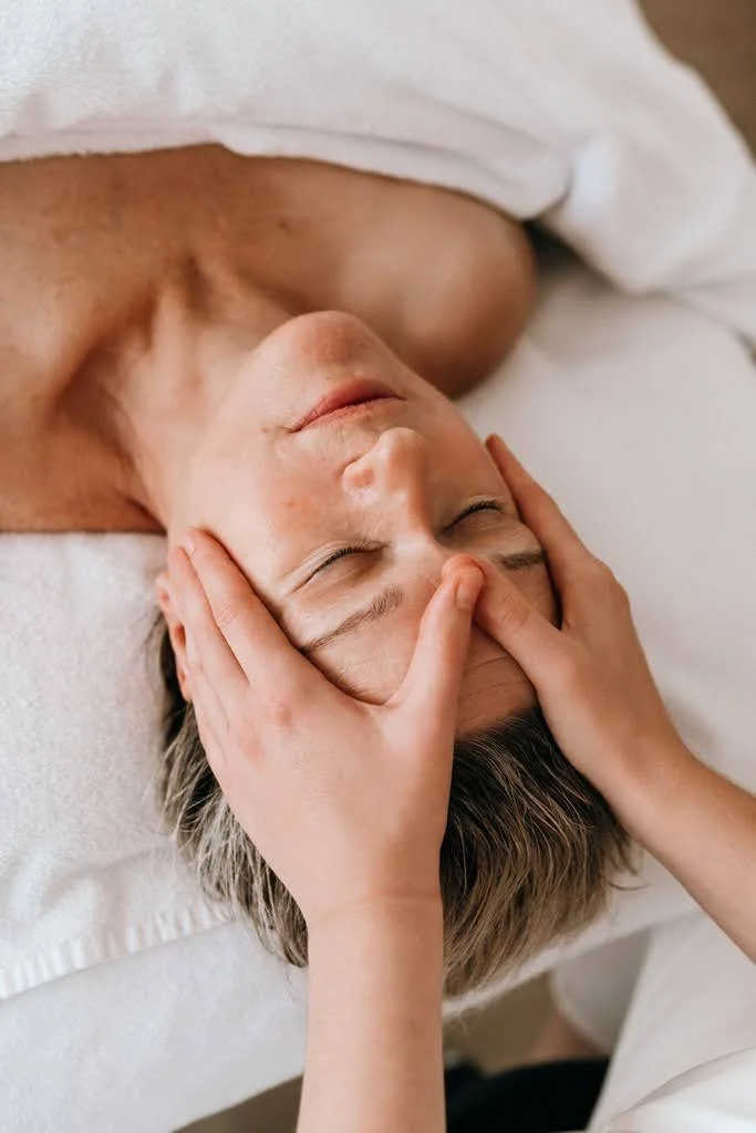 Une personne reçoit un massage du visage par un praticien dans un cadre relaxant.