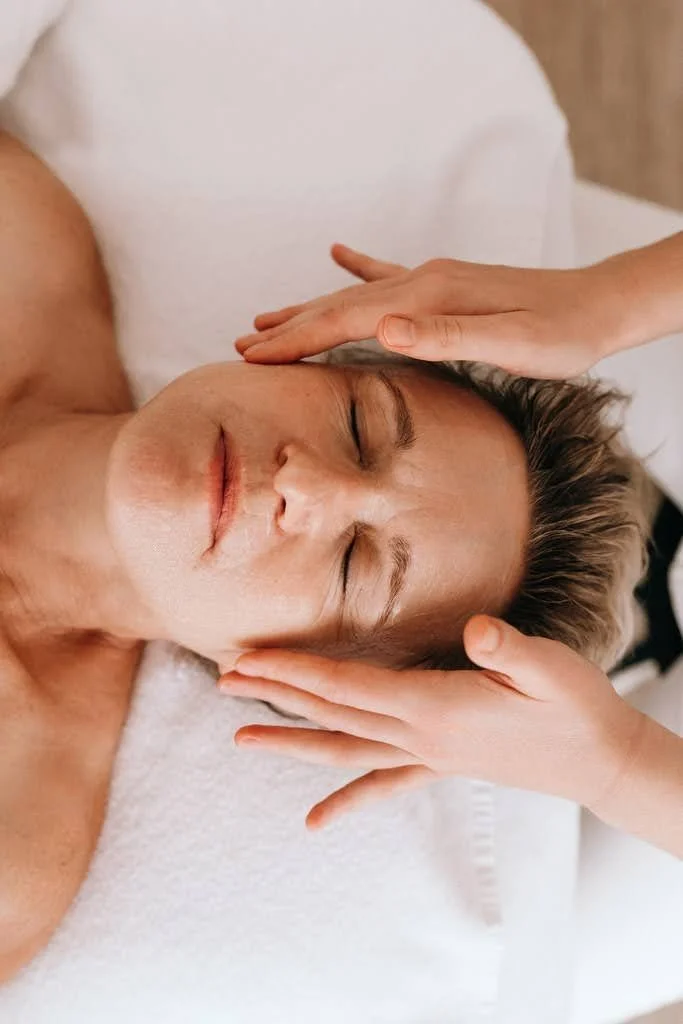 Une personne reçoit un massage de la tête, casque, visage détendu.
