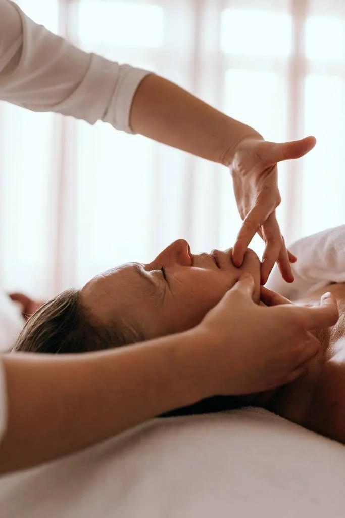 Une femme reçoit un massage facial, une autre personne touche son visage avec ses doigts.