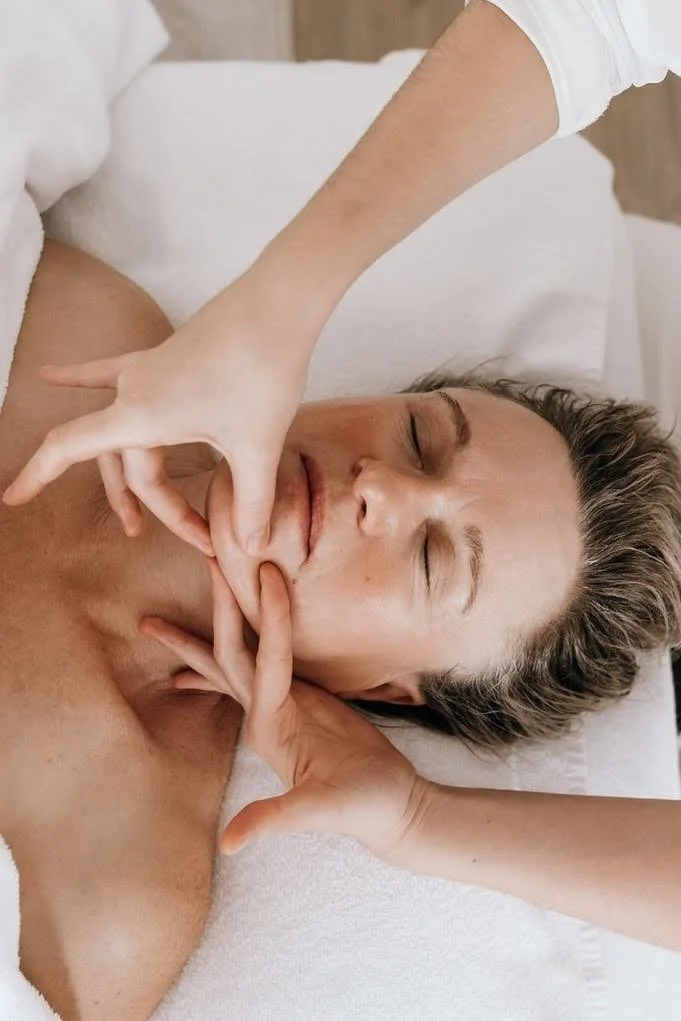 Une personne reçoit un massage du visage dans un cadre relaxant, allongée sur une surface blanche