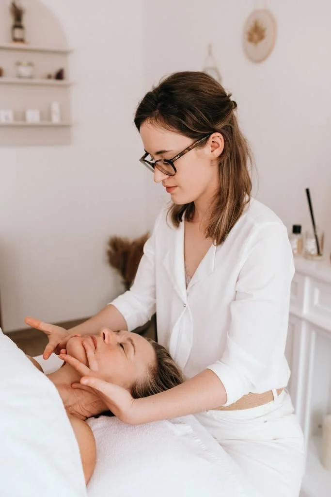 Une esthéticienne effectue un soin facial sur une cliente allongée dans un salon de beauté lumineux.