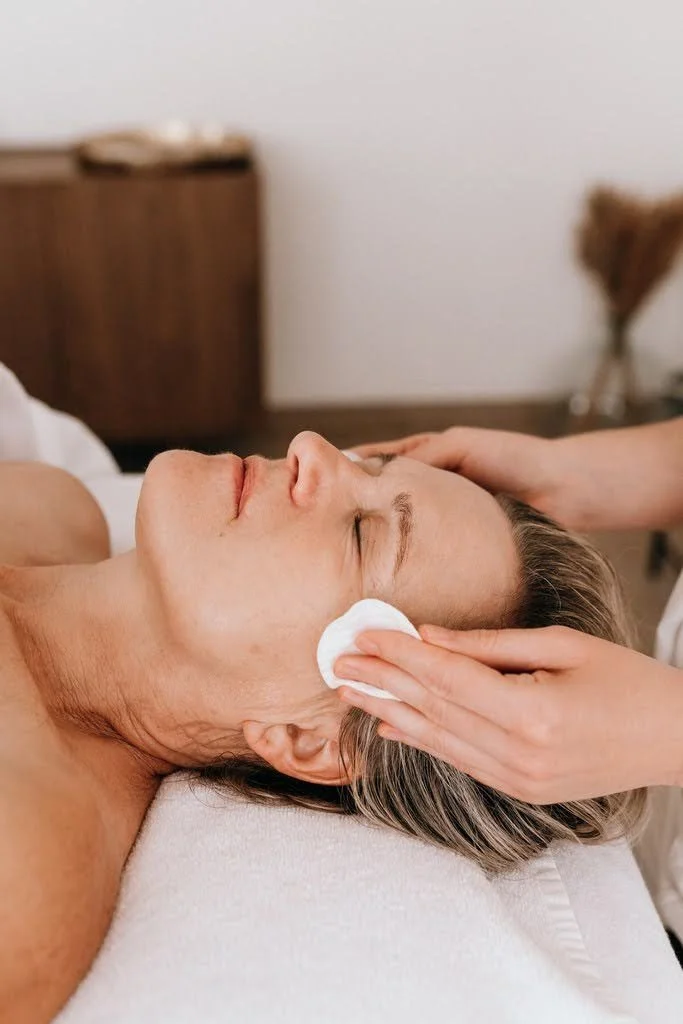 Une femme reçoit un soin du visage, une personne nettoie ou hydrate sa peau avec un disque de coton.