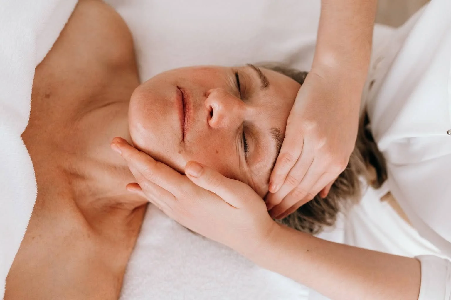 Une personne reçoit un massage facial relaxant, les yeux fermés, dans un cadre apaisant.