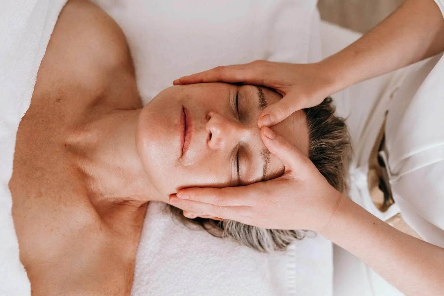 Une personne reçoit un massage facial relaxant d'une thérapeute dans un cadre de spa.