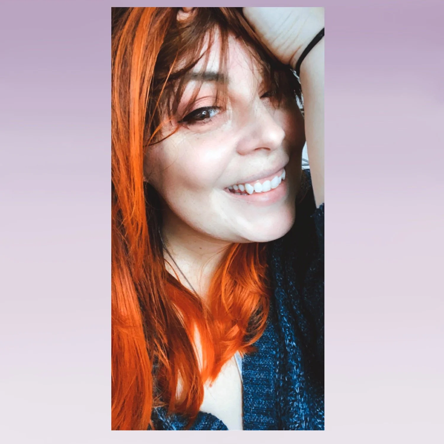 Woman with long orange-red hair smiling at camera while running her hand through her hair