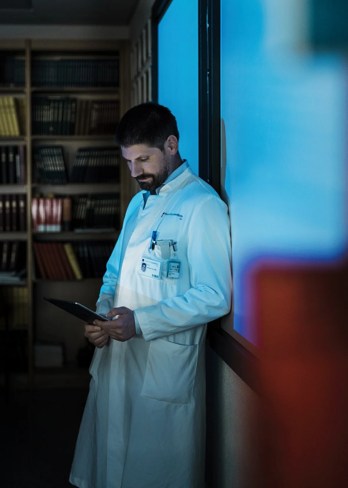 Prof. Dr. med. Sebastian Kuhn lehnt an eine Wand mit blauem Licht und schaut in ein Tablett n der Mainzer Uniklinik: Wissenschaftsfotografie von Angelika Zinzow