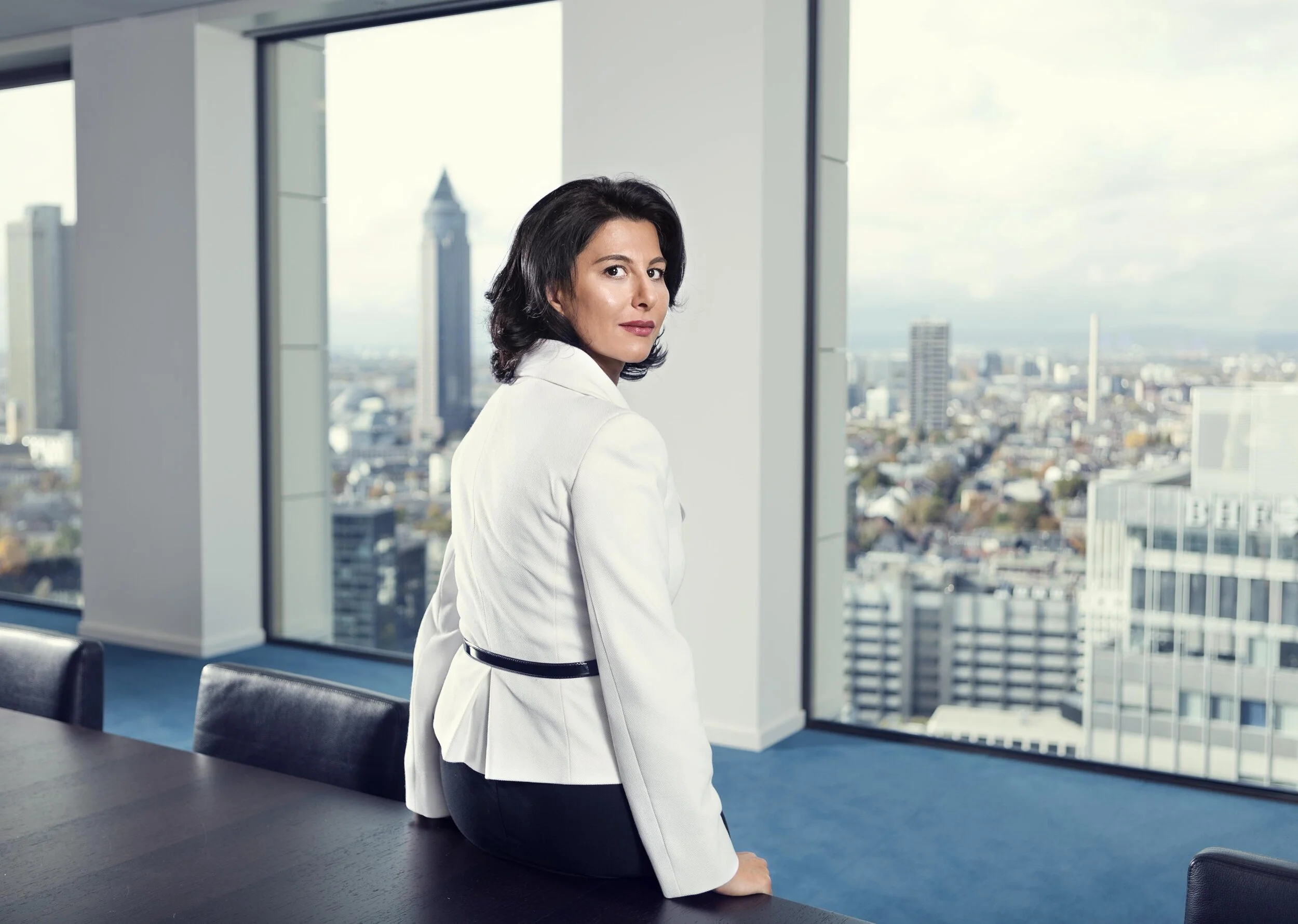 Selina Piening schaut über ihre Schulter in die Kamera, im Hintergrund ist eine Fensterfront mit Blick auf eine Stadt zu sehen: Business Portrait von Angelika Zinzow
