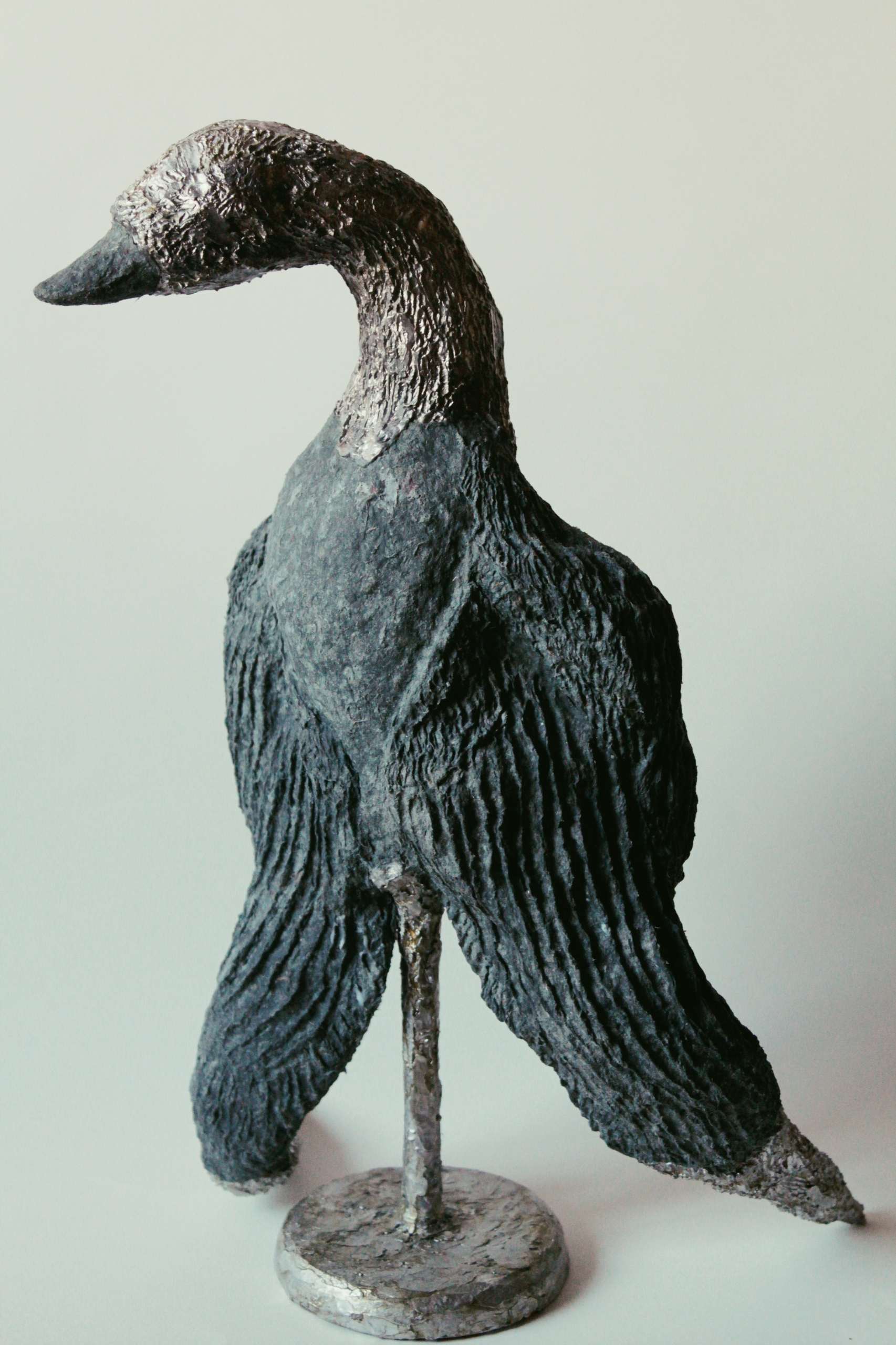 Skulptur eines Pinguins aus schwarzem und silbernem Material, stehend auf einem runden Sockel.