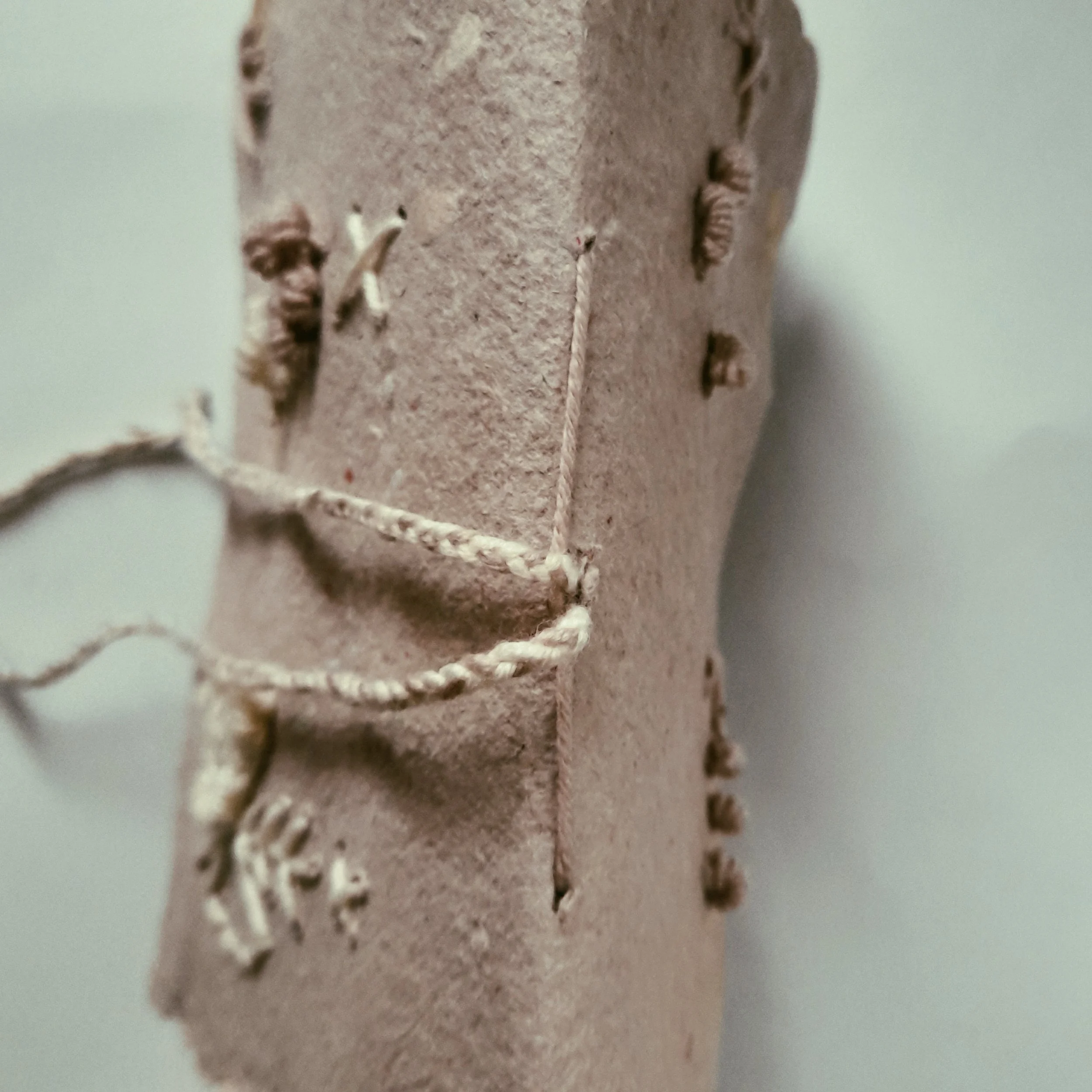 Detaillierte Nahaufnahme von einem Stück brauner Pappe mit eingeritztem Muster aus Fäden und Papierschnipseln.