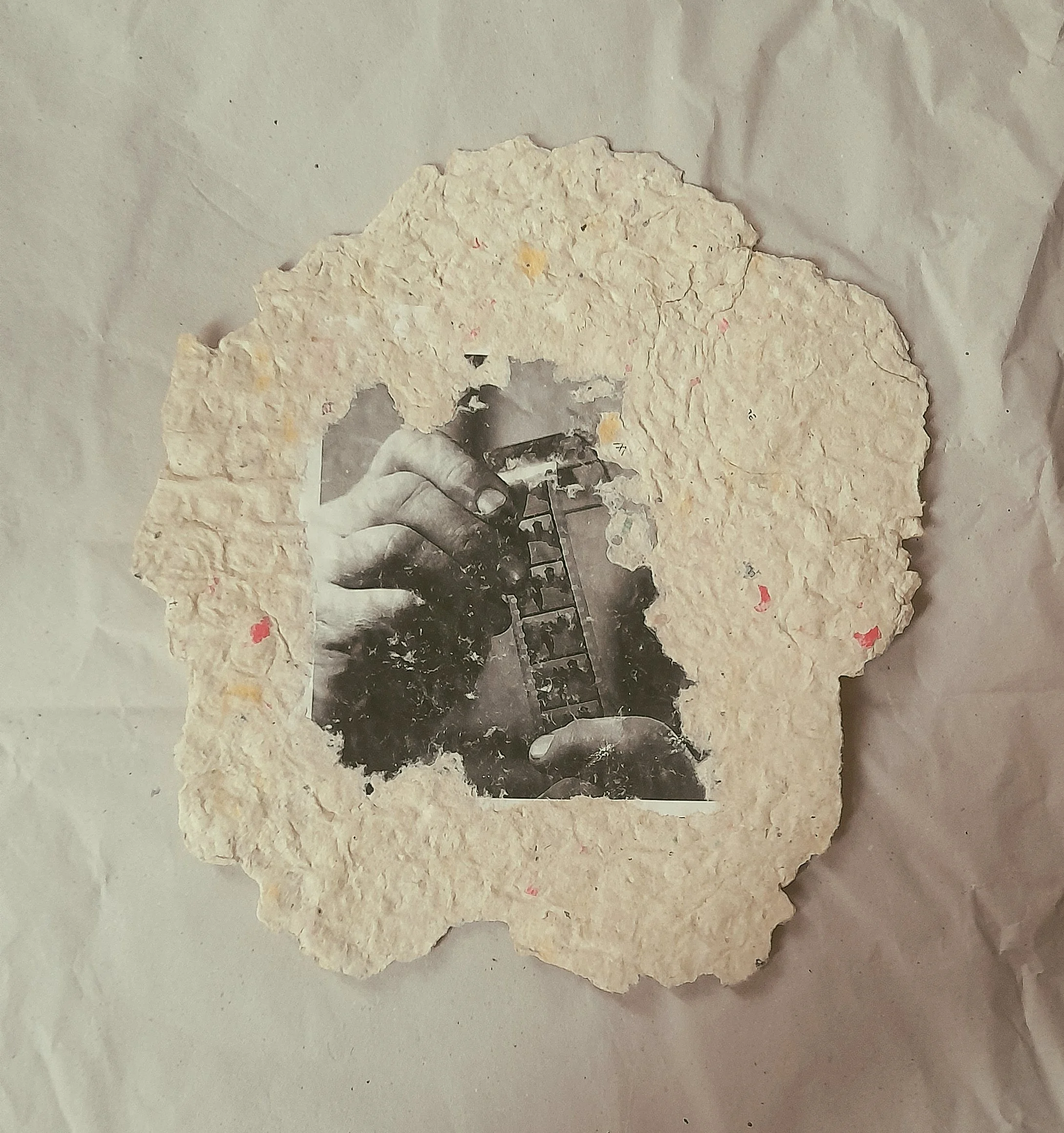 Ein unregelmäßig geformtes handgeschöpftes Papier  mit einem schwarz weiß Foto einer Hand, die eine Filmrolle hält