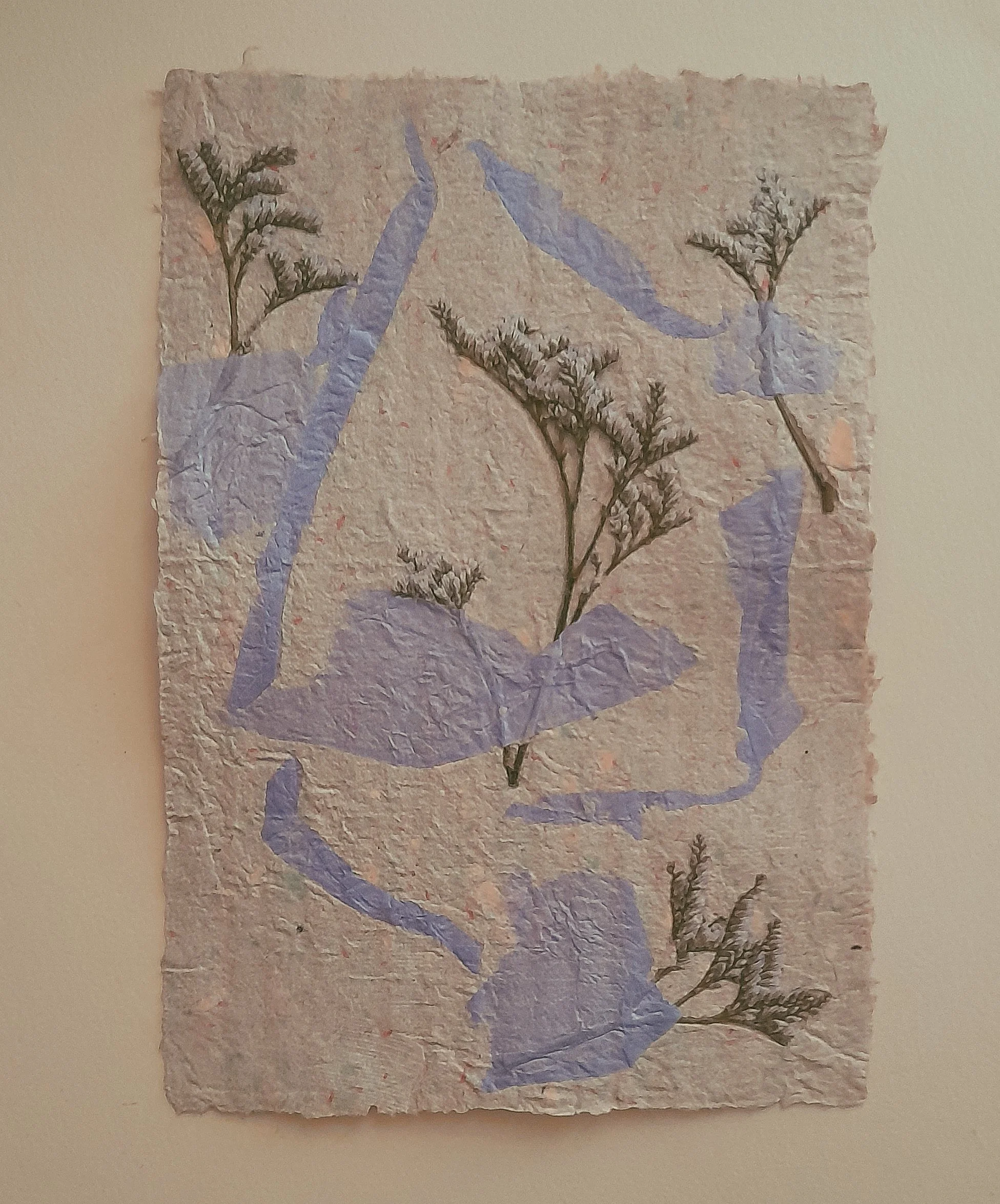 Trockenes, grobes Papier mit eingelegte getrocknete Blumen und lila Bänder.