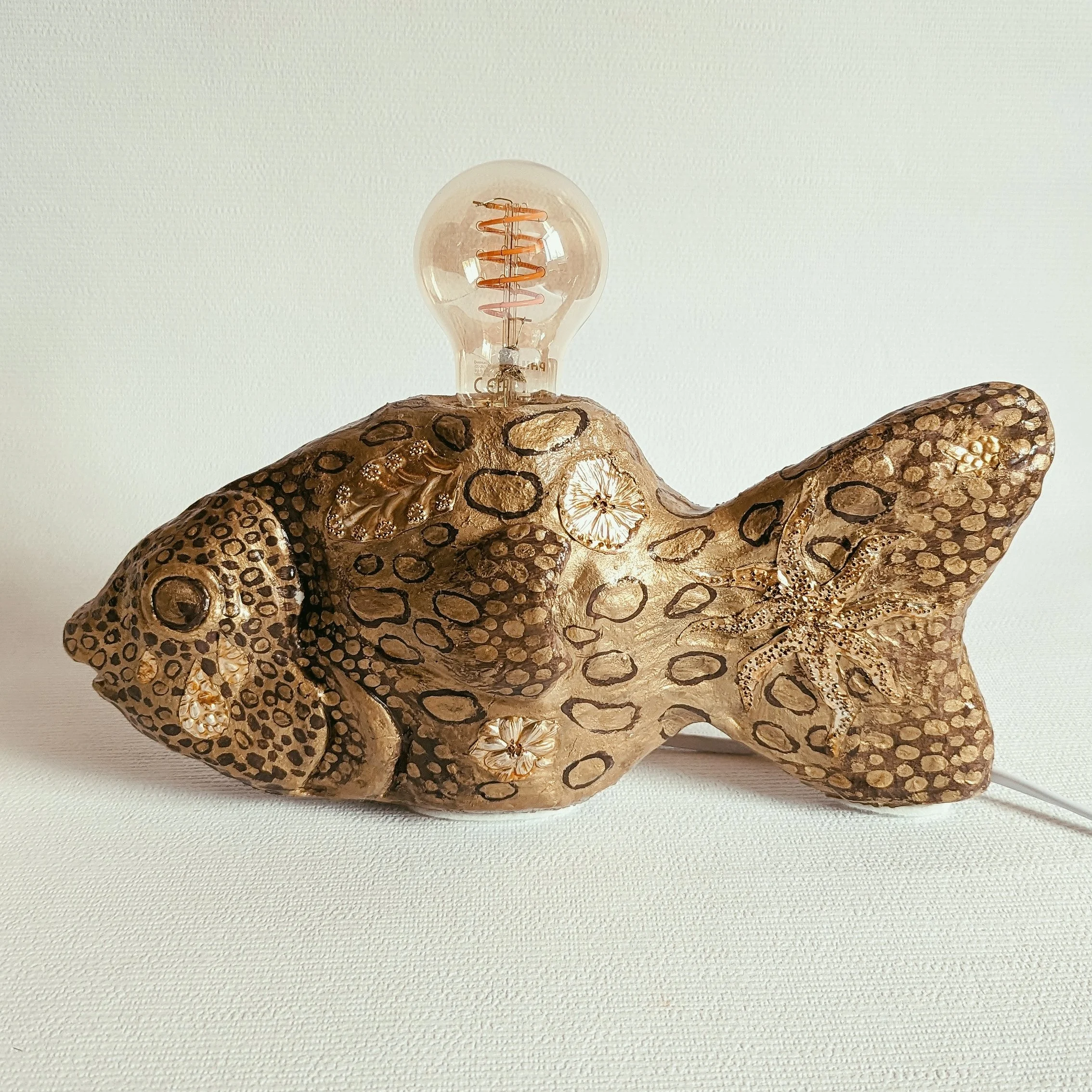 Eine Glühbirne steht auf einer dekorativen, braunen, geprägten Holzskulptur, die wie ein Reptil oder Echse aussieht, vor einem weißen Hintergrund.