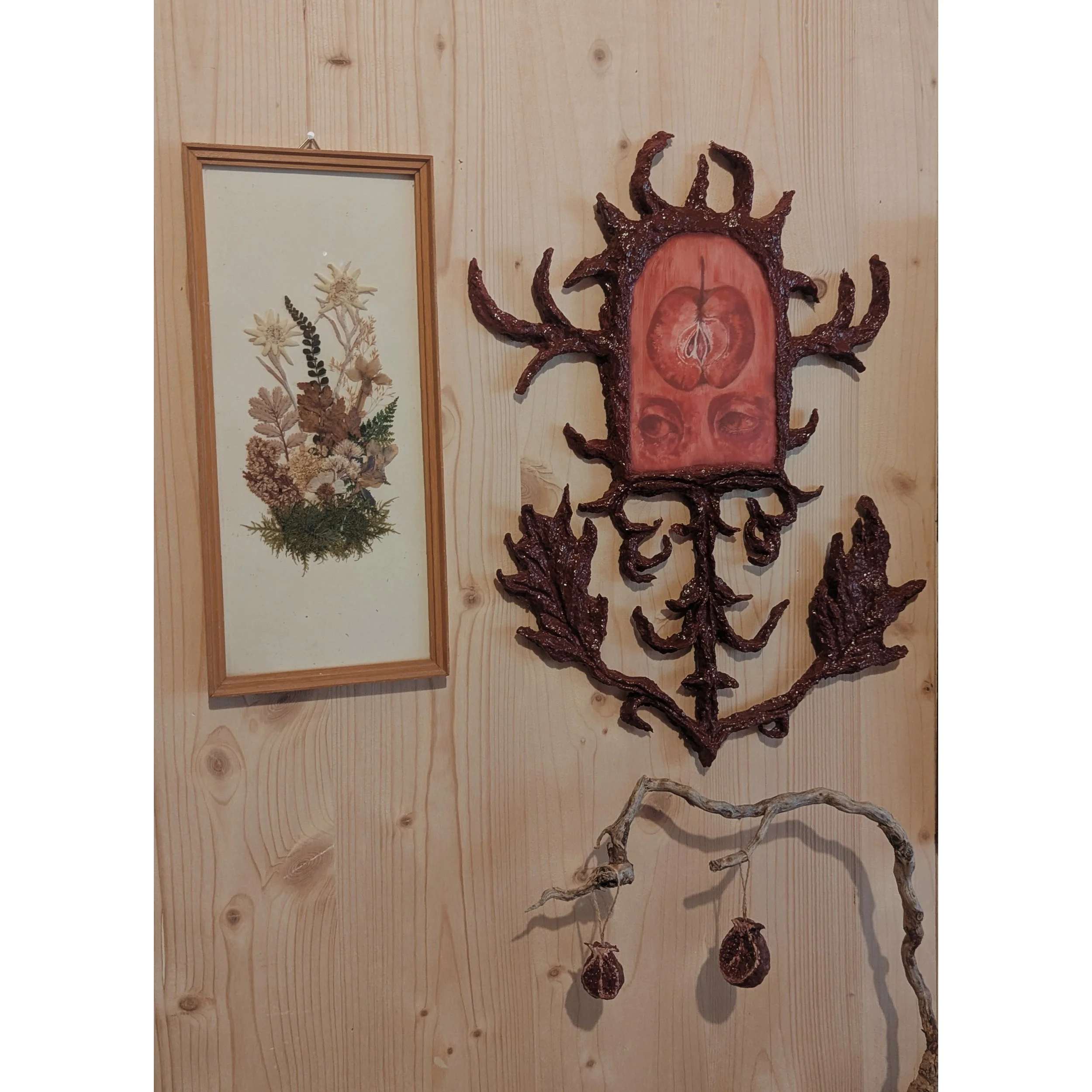 Kunstwerk aus roten und braunen Wurzeln oder Ästen, gestaltet wie ein abstraktes Gesicht mit mehreren Armen, an einer Holzvertäfelung.