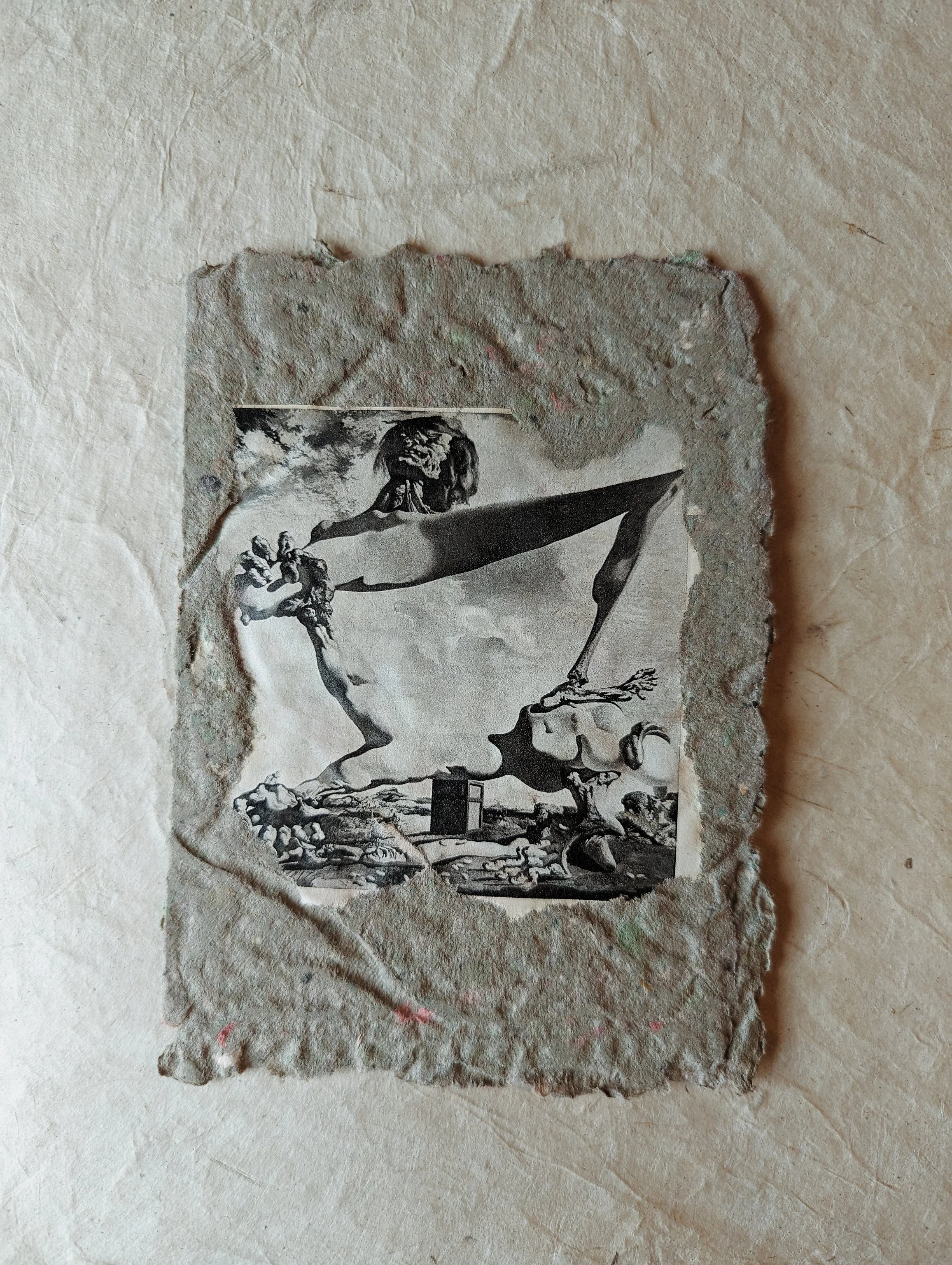 Schwarz-weiß-Foto auf einem groben, unregelmäßigen Papierstück, zeigt eine fantasievolle Szene mit einer menschlichen Figur, die einen langen Arm hat, der eine bunte Figur hält, mit einem natürlichen Hintergrund.