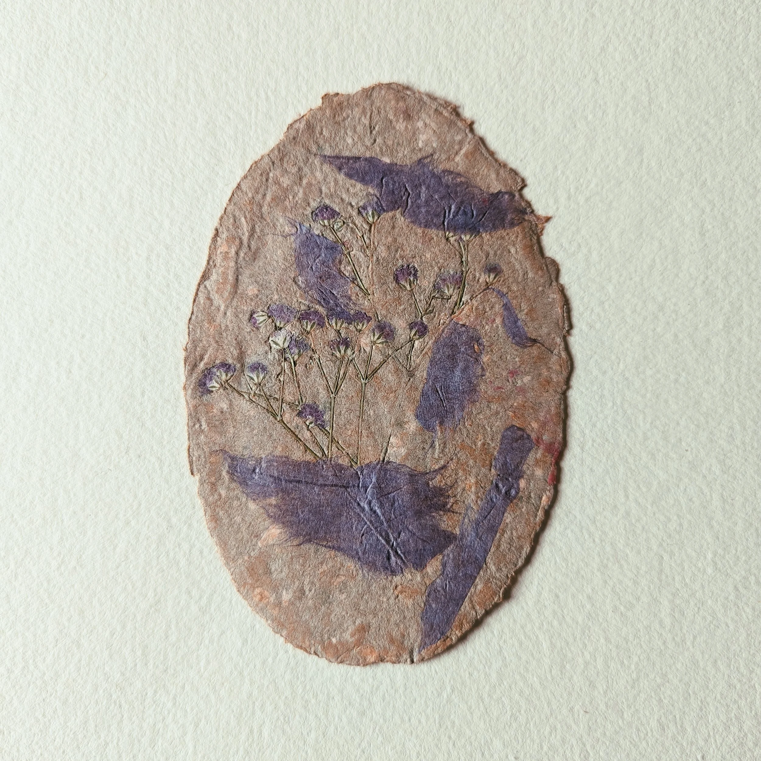 Ein unregelmäßig geformtes eiförmiges Papier handgeschöpftes Papier  mit eingearbeiteten, getrockneten Blumen und Blättern.