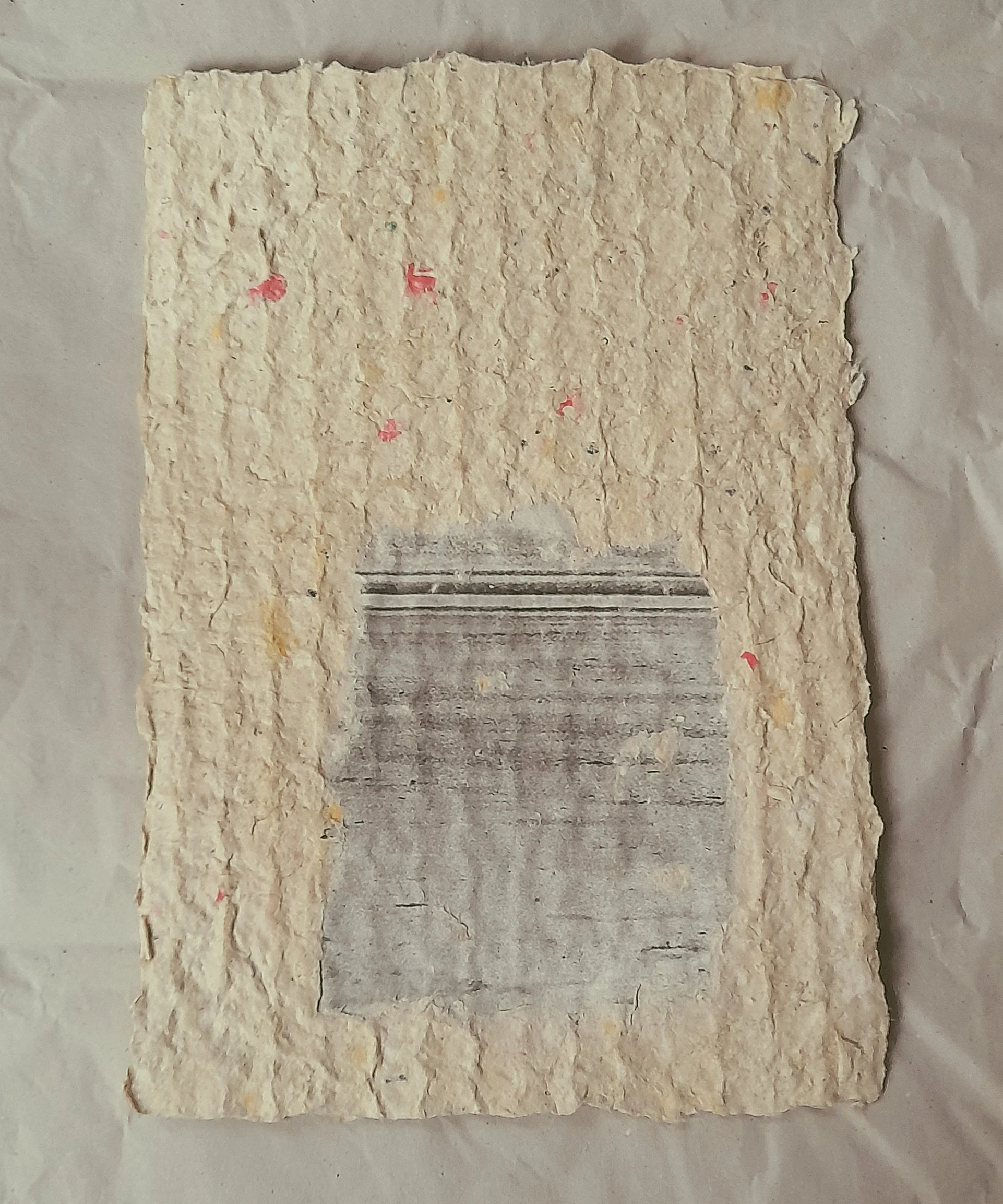 Ein rauhes handgeschöpftes Papier, cremefarbene Papier mit einem Druck eines grauen, mit Linien verzierten Objekts, der auf einer Papierrückseite liegt.