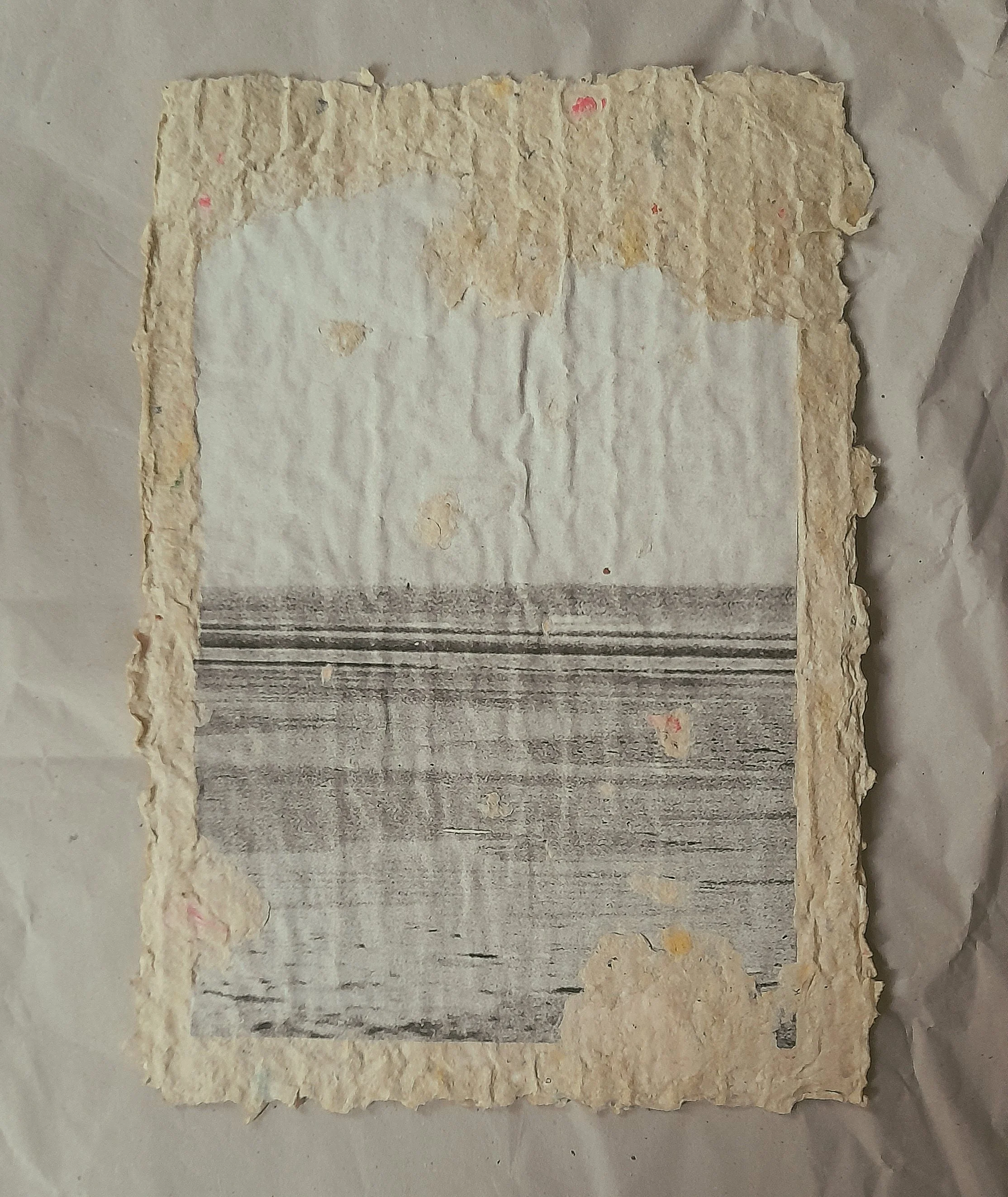 Ein handgeschöpftes Papier mit Rissen und verblasstem Druck, umgeben von bräunlichem, rauem Papier.