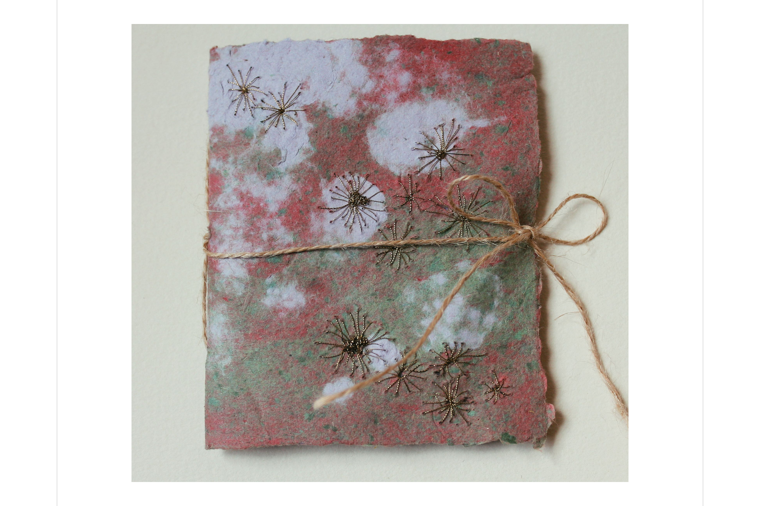 Ein handgemachtes Geschenk mit bunt marmoriertem Papier, verziert mit kleinen metallischen Schneeflocken und mit einem Juteschnur zugebunden.