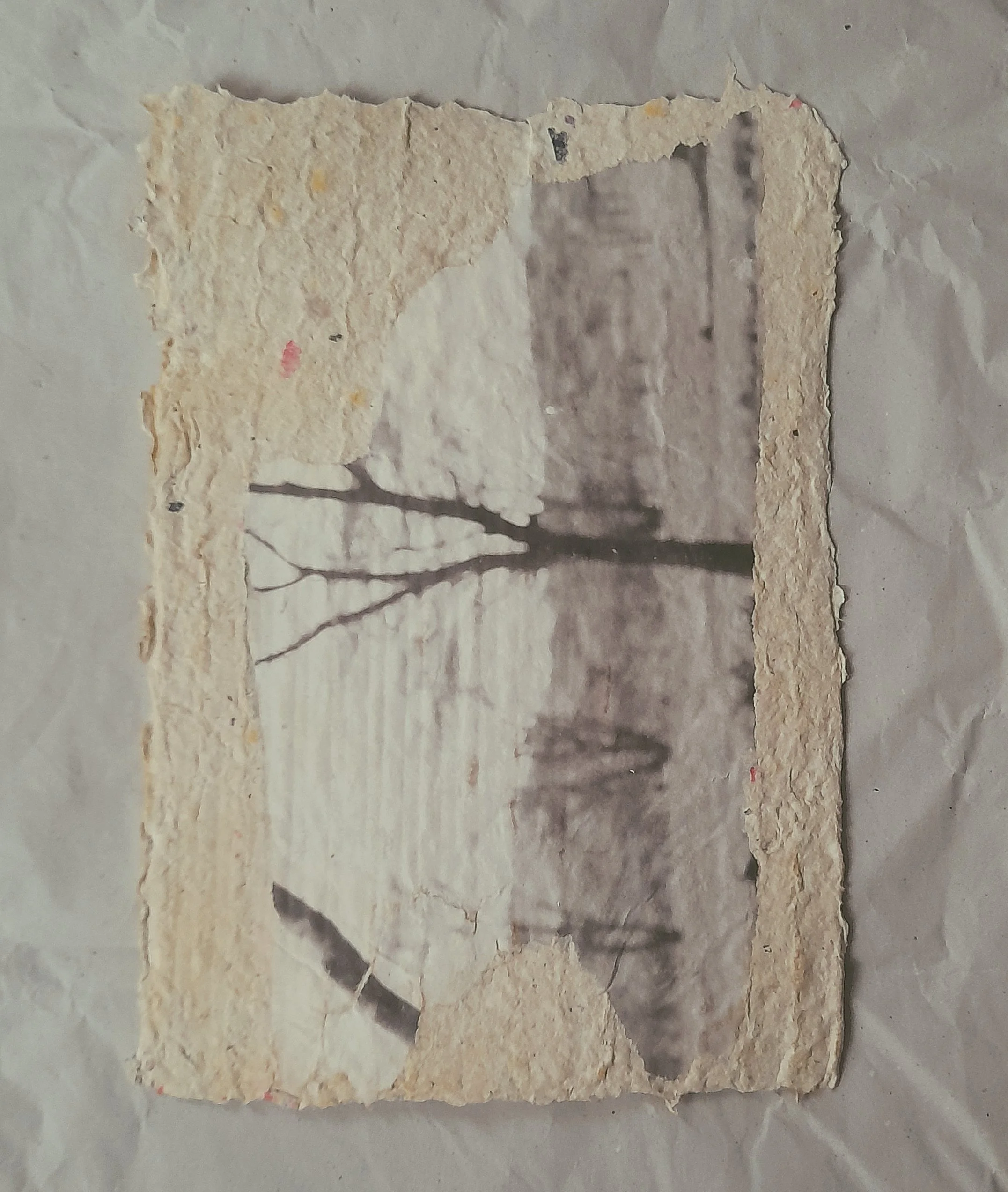 Ein handgeschöpftes Papier mit einem eingearbeiteten Motiv schwarz weiß  eines Baumes in einer ländlichen Umgebung, das teilweise zerfällt.