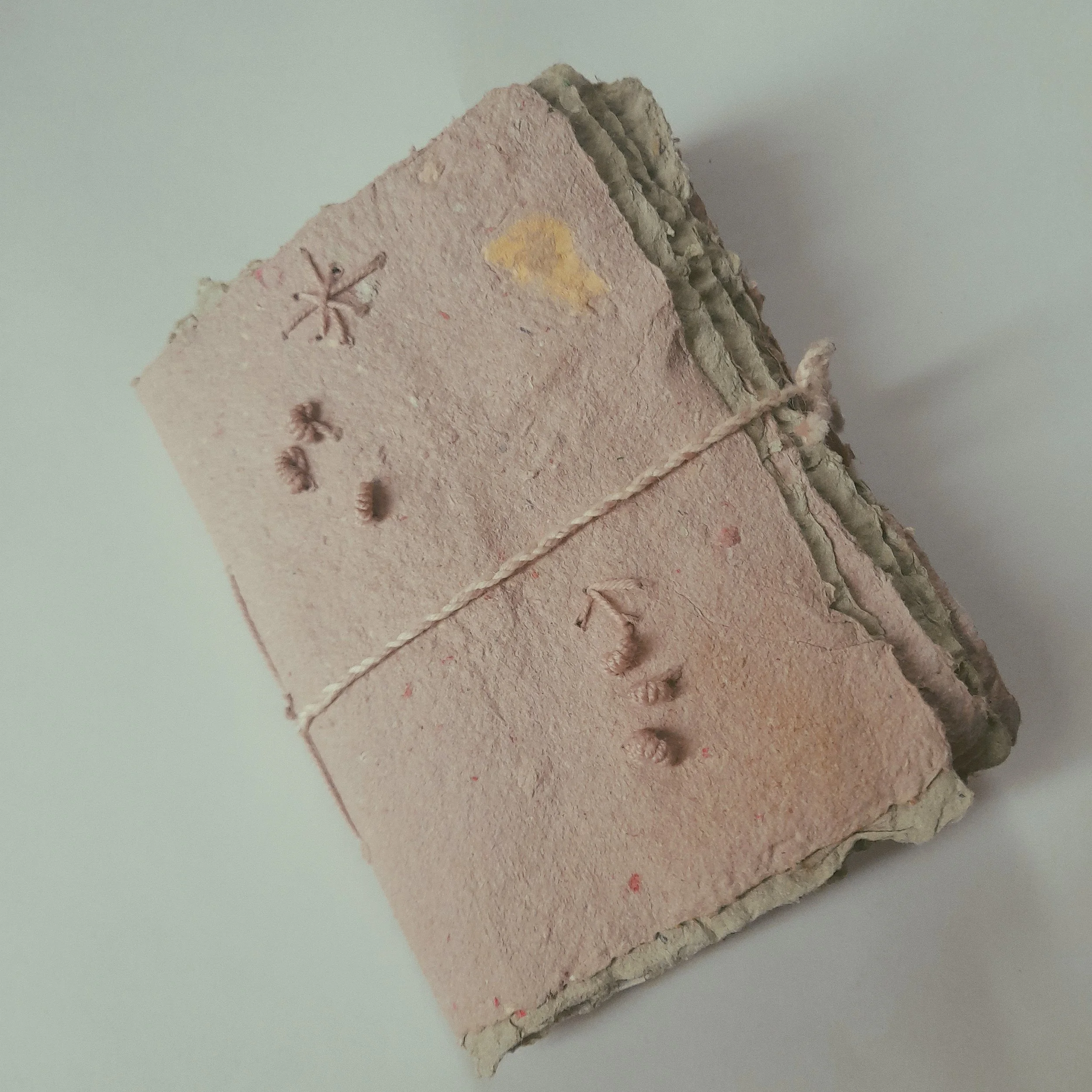 Ein Bündel handgefertigter Papierbücher, gebunden mit einem Faden, mit sichtbaren Naturmaterialien und Handarbeitselementen auf dem Cover.