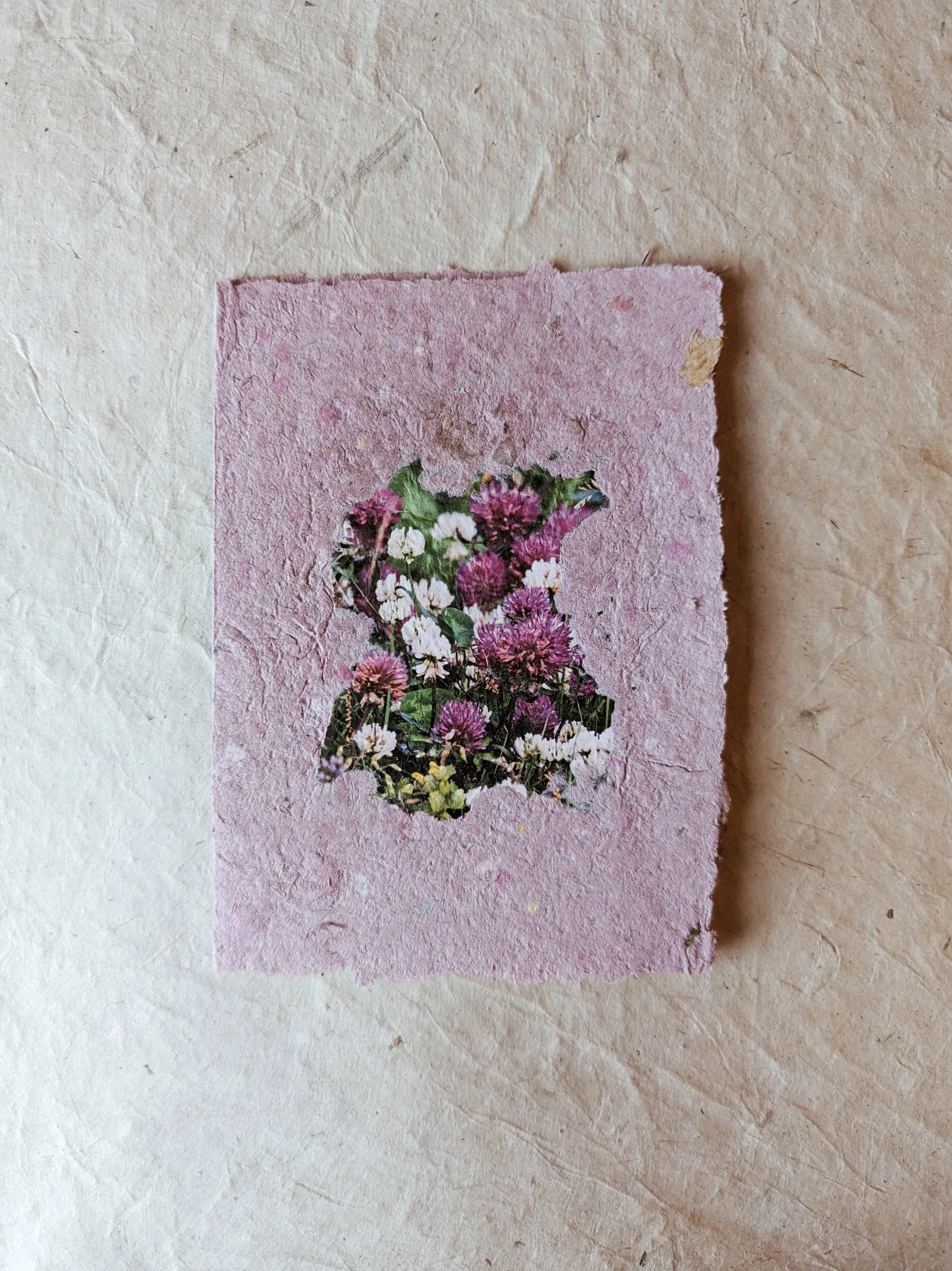 Braune Papierkarte mit einer Schneidekante und einem Muster aus verschiedenen Blumen in pink, violett und weiß, das die Form eines Tieres bildet.