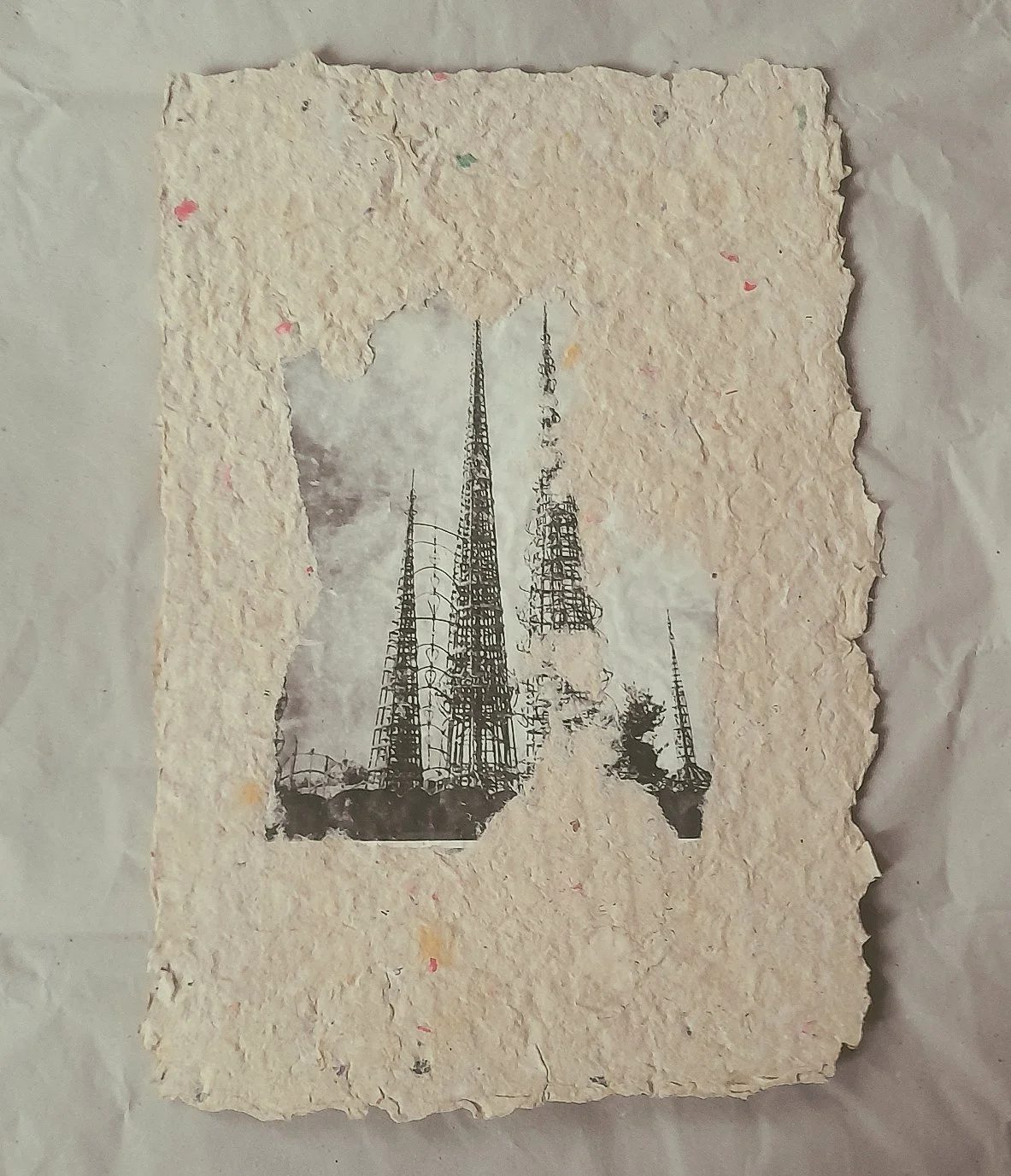 Ein Gemälde auf einer handgemachten Papierkarte zeigt eine Stadtsilhouette mit hohen Türmen, in Schwarz-Weiß gehalten.
