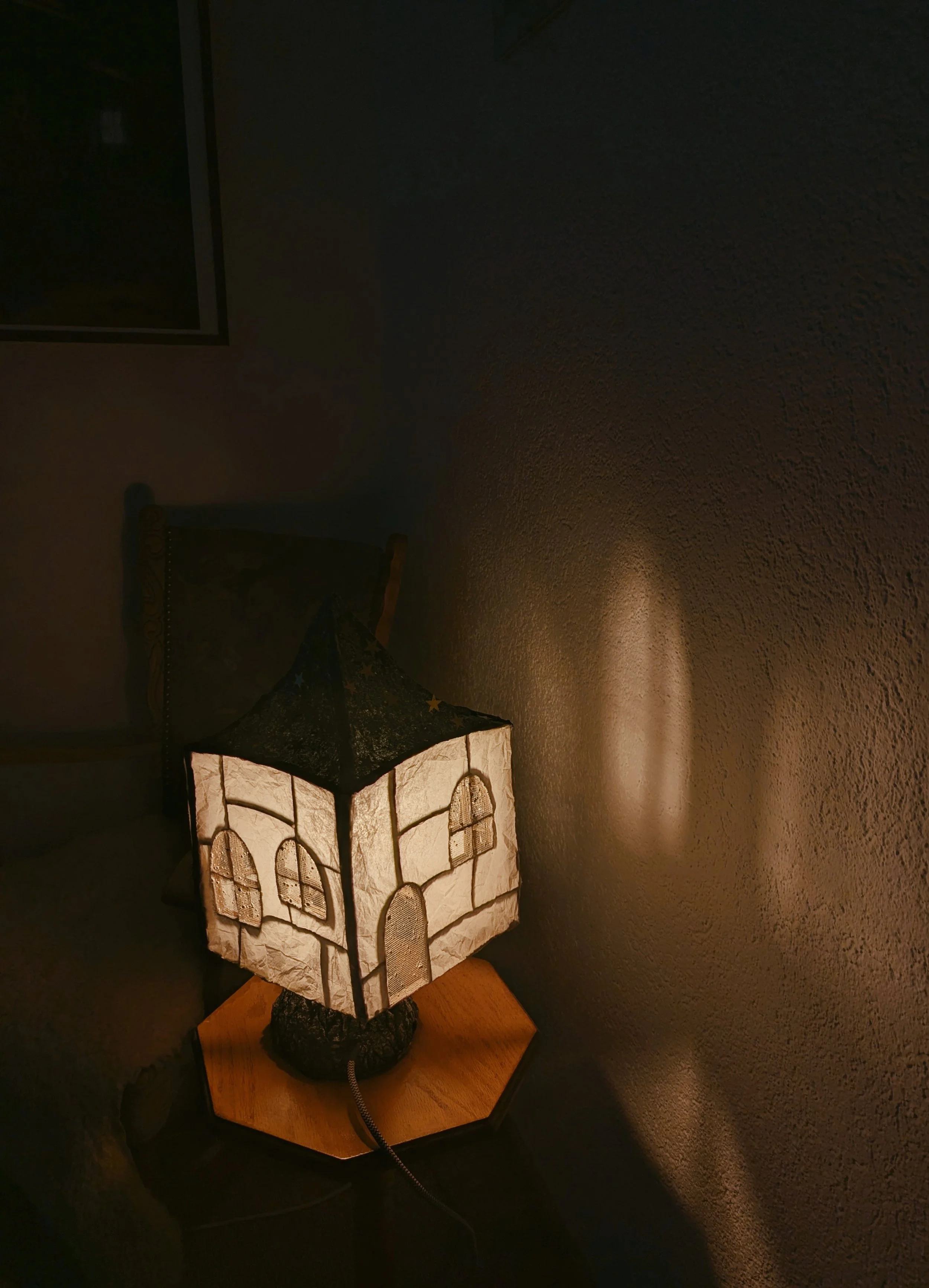 Ein Stehlampe mit einem Körbchen-Design, das warmes Licht ausstrahlt, steht auf einem Holztisch neben einer dunklen Wand.